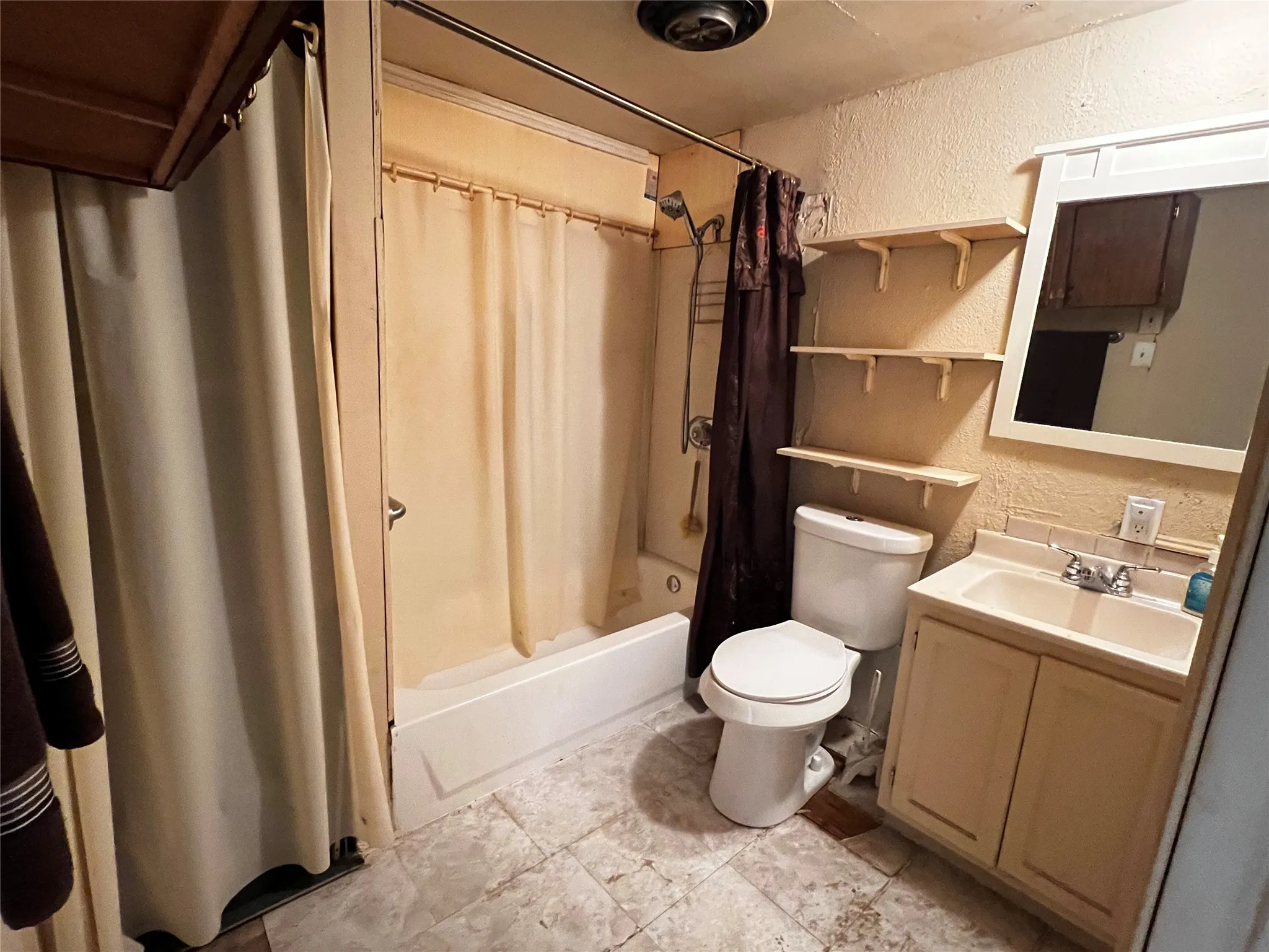 Bathroom featuring a shower-tub combination, a vanity with an integrated sink, a wall-mounted mirror, open linen closet, and open shelving