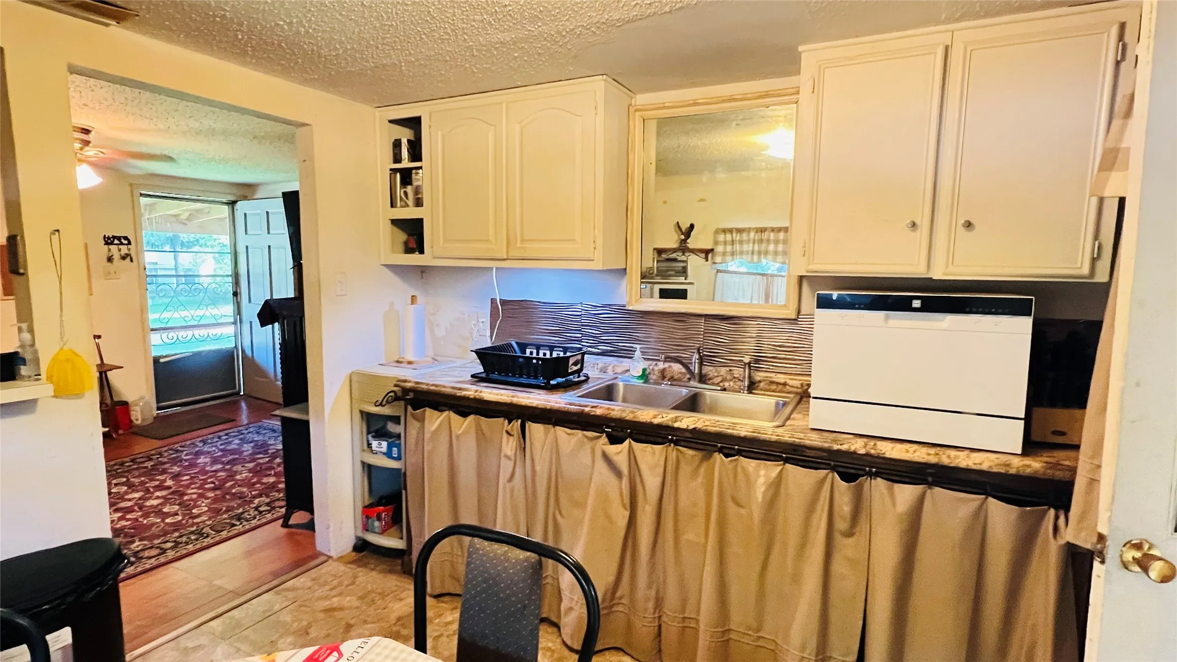 Kitchen area featuring cream cabinetry, a double basin sink, and a laminate countertop with a stone-look finish