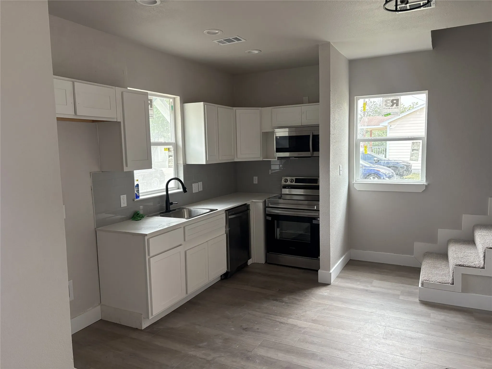 Modern kitchen featuring white cabinetry, light gray countertops, stainless steel appliances, a black gooseneck faucet, and wood-finish flooring