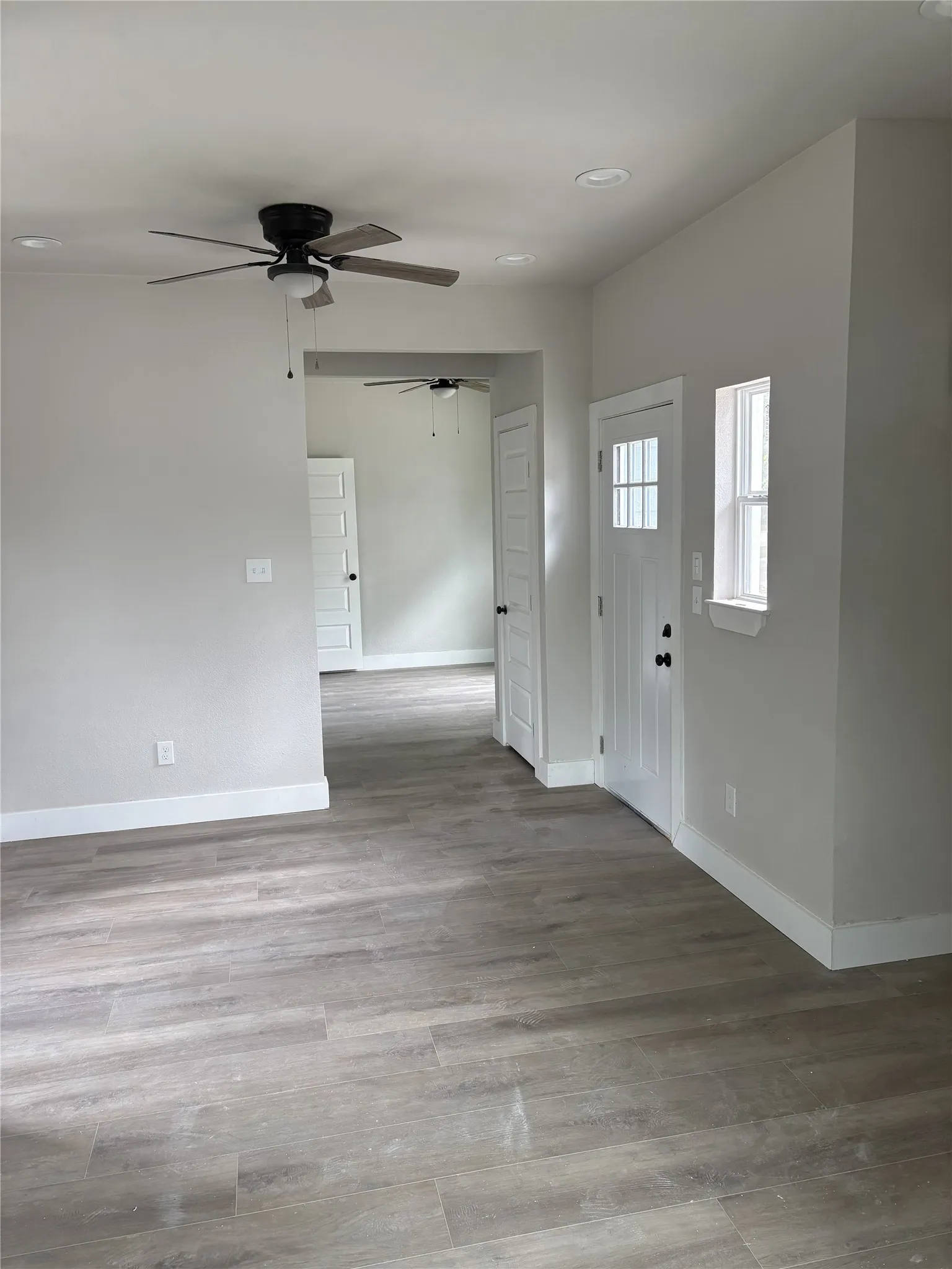 Light-filled interior featuring wood-finish flooring, recessed lighting, ceiling fan, white baseboards, and a paneled front door with divided lites