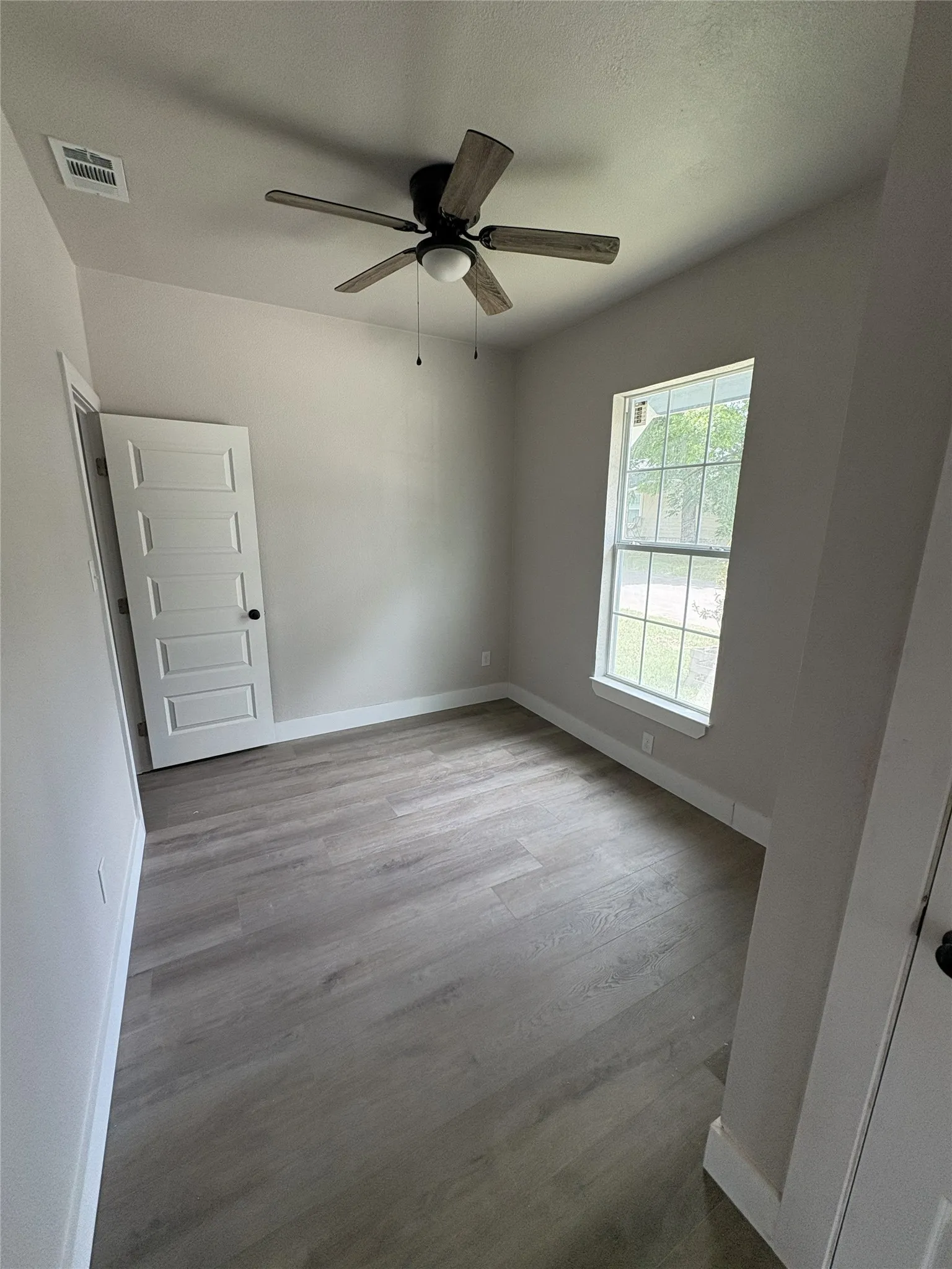 Neutral-toned interior featuring wood-finish flooring, a ceiling fan with light, and a paneled door