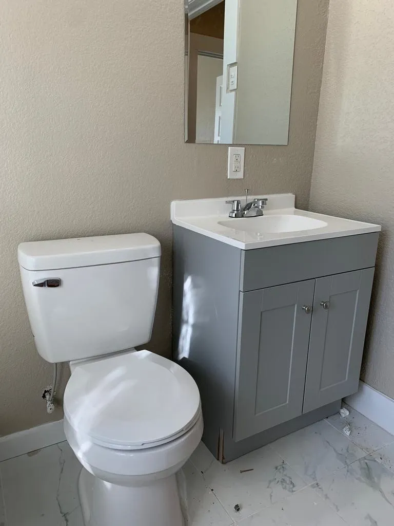 Bathroom featuring a gray shaker-style vanity with a white integrated sink, chrome faucet, and coordinating mirror