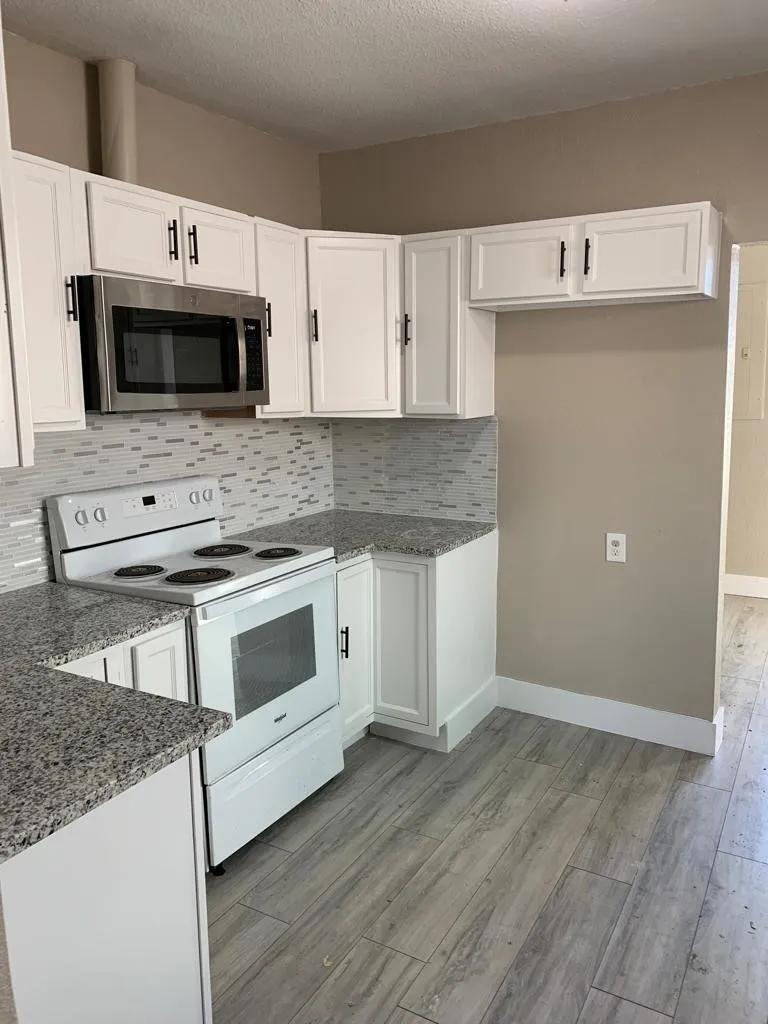 Kitchen featuring white cabinetry with black hardware, light-toned granite-style countertops, mosaic tile backsplash, and wood-finish flooring