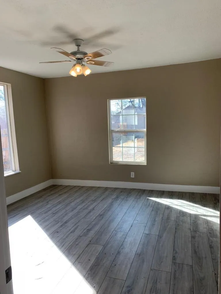Spacious room featuring wood-finish flooring, two windows, baseboard trim, and a ceiling fan with integrated lighting