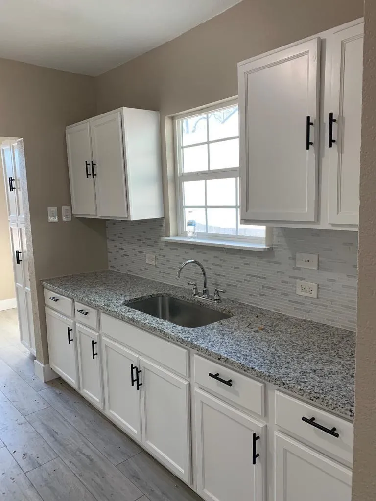 Kitchen featuring white shaker-style cabinetry with matte black hardware, granite countertops, and a stainless steel sink