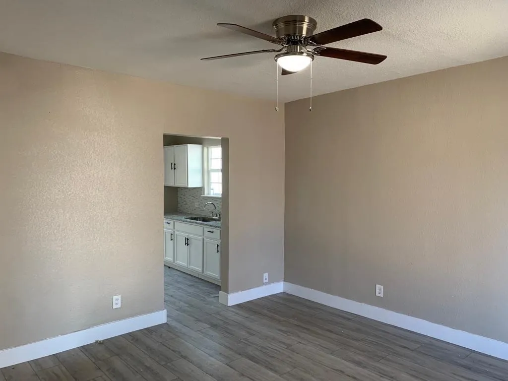 Open-concept living area featuring wood-finish flooring, a ceiling fan with integrated lighting, and neutral wall tones