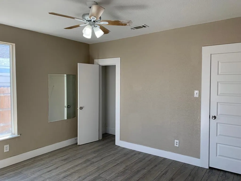 Interior space featuring wood-finish flooring, a ceiling fan with integrated lighting, and a window with white trim