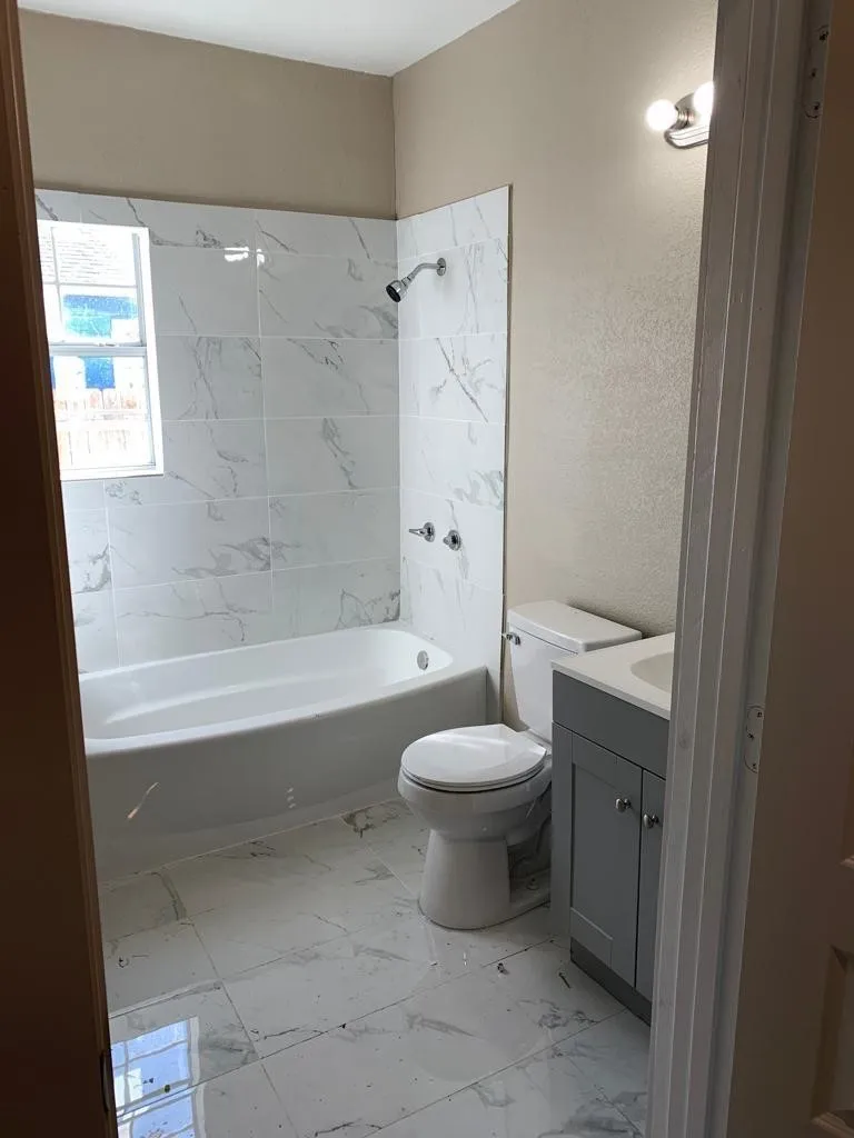 Bathroom featuring a white bathtub, marble-look tile flooring, and a matching tile shower surround