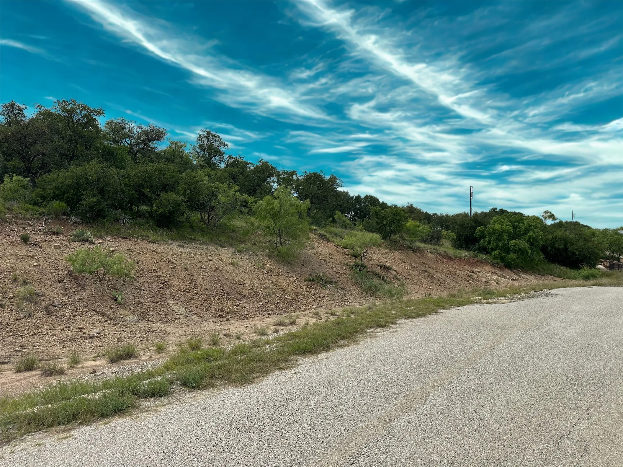 Expansive undeveloped terrain featuring a gravel road, natural vegetation, and a rolling hillside