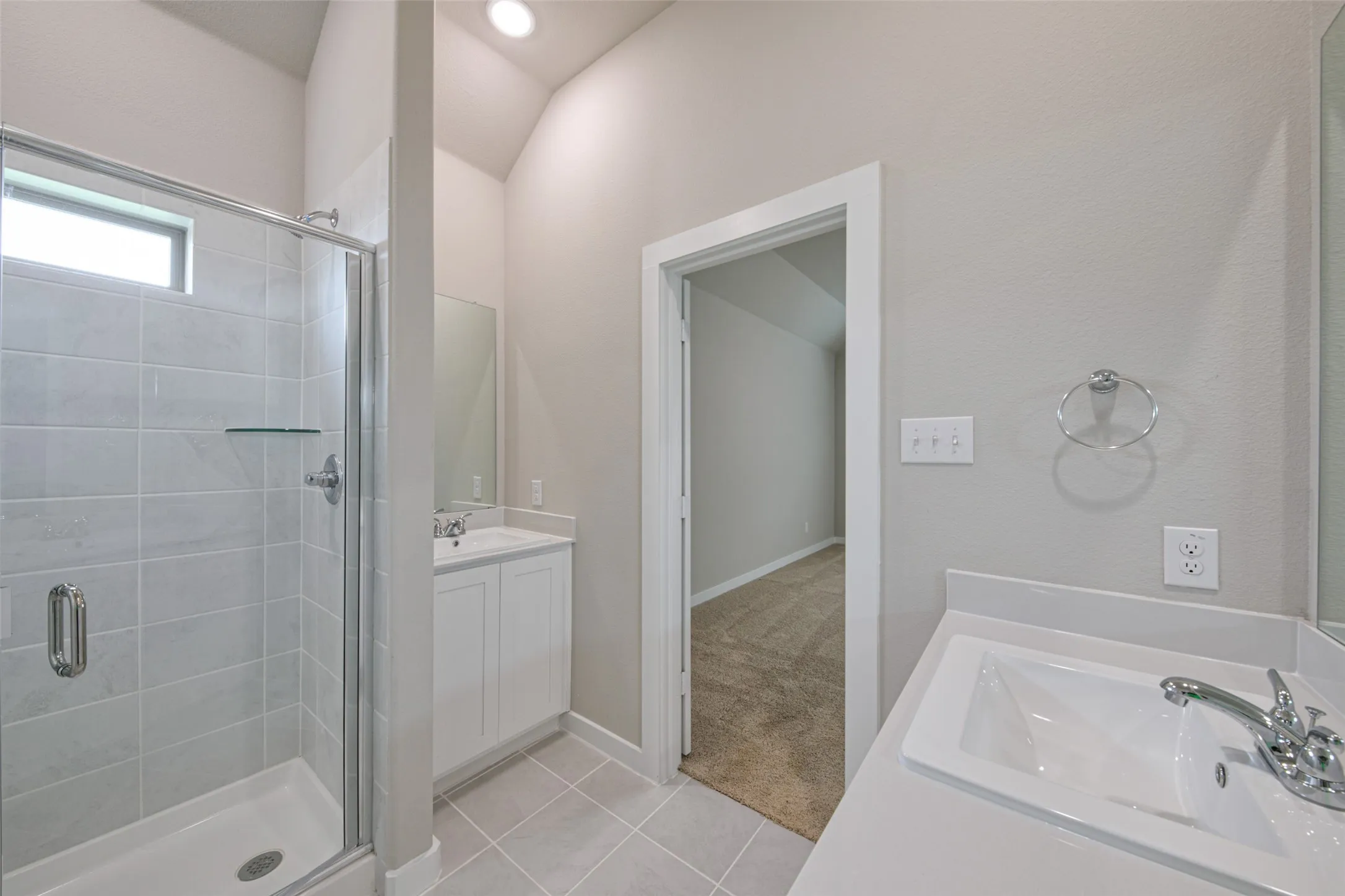 Bathroom featuring a glass-enclosed shower with tile surround, dual vanity sinks with white cabinetry, and light-toned floor tiling
