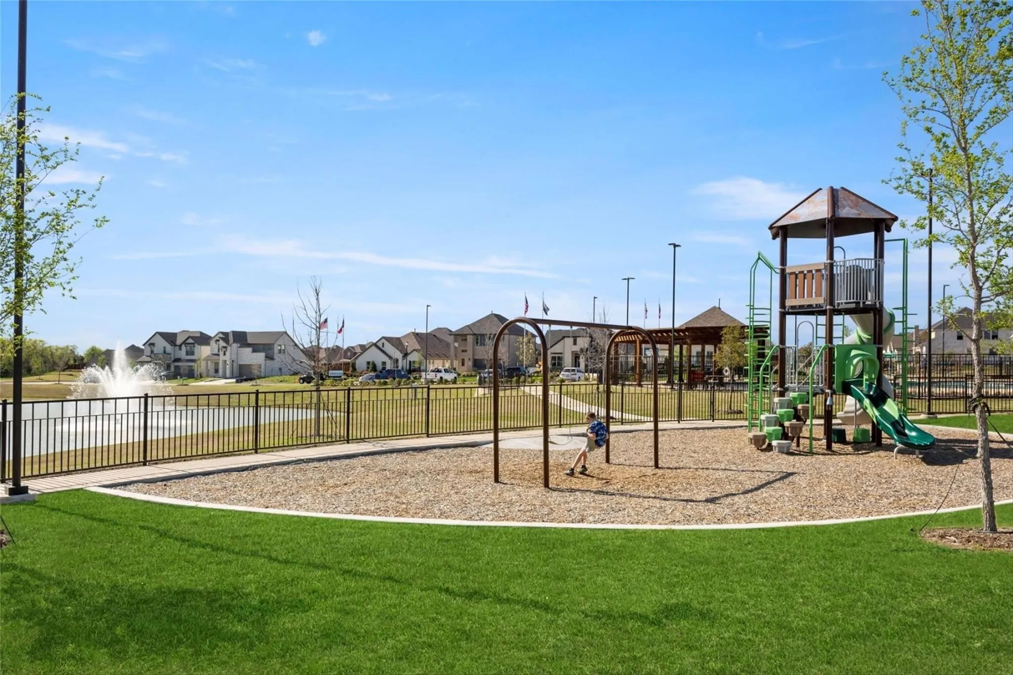 Community playground featuring a swing set, multi-level play structure with slide, and a wood chip surface