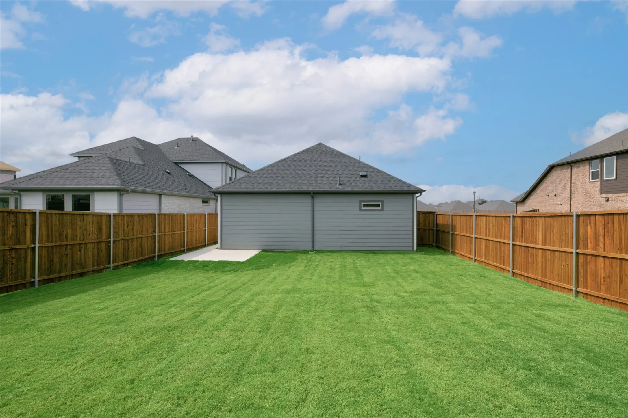 Spacious backyard featuring a manicured lawn, full wood fencing, and a concrete patio pad