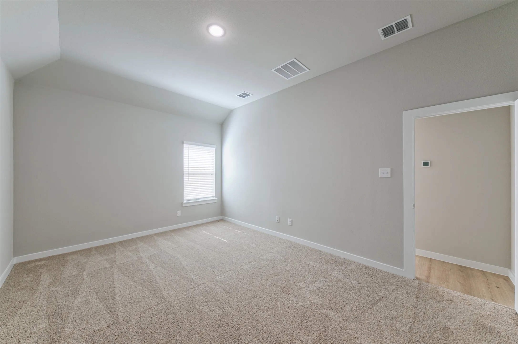 Spacious room featuring vaulted ceilings, neutral-toned carpeting, and a window with blinds