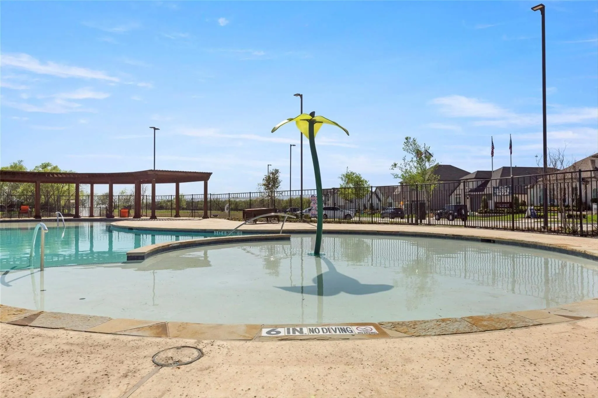 Community swimming pool featuring an integrated splash pad with a water play feature, a separate lap pool, and a shaded pergola area