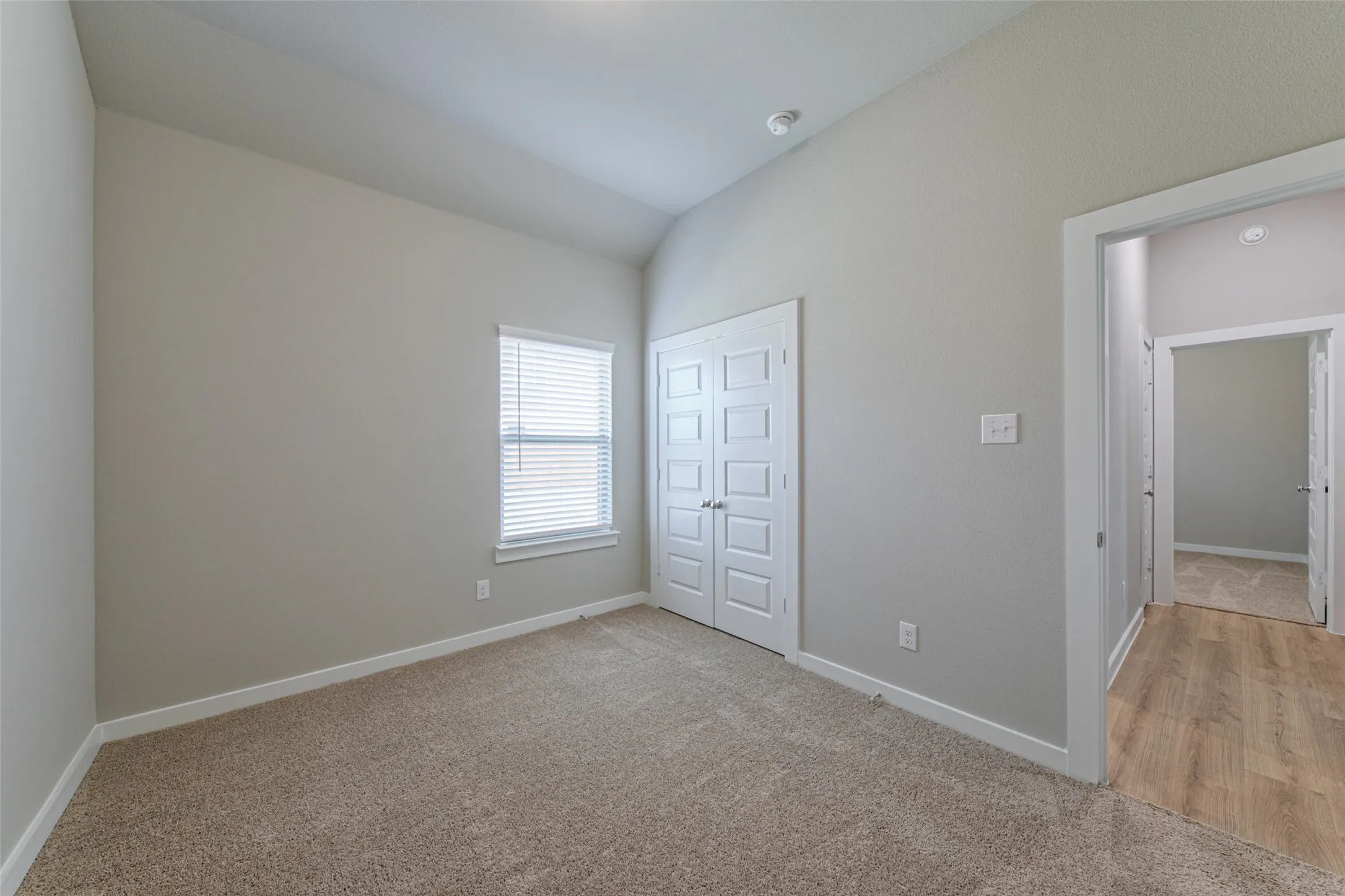 Neutral-toned interior featuring vaulted ceilings, carpet flooring, and a window with blinds