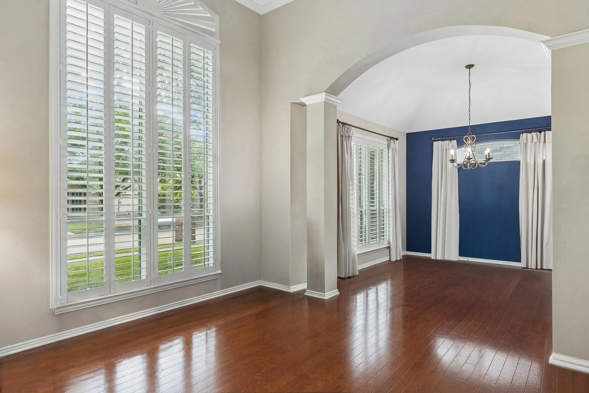 The living room enjoys abundant natural light from oversized windows with Plantation Shutters. Gleaming hardwood flooring completes the space. The graceful arched opening with pillars gives definition to the dining room.