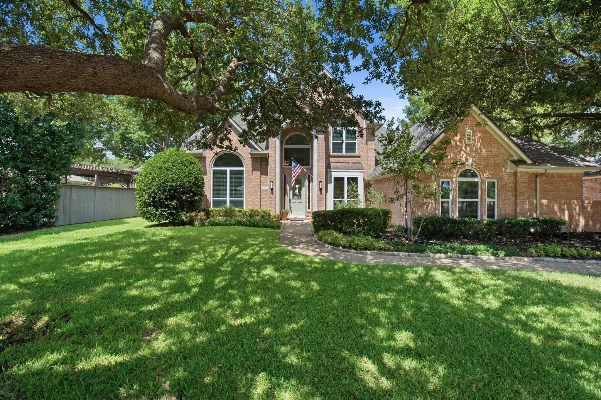 Brick facade with arched windows, mature trees, and a manicured lawn