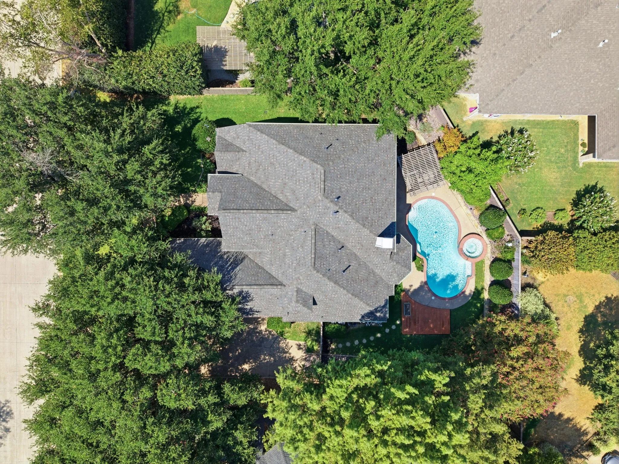 Architectural shingle roof, freeform swimming pool with integrated spa, wood pergola, expansive green lawn, and mature trees