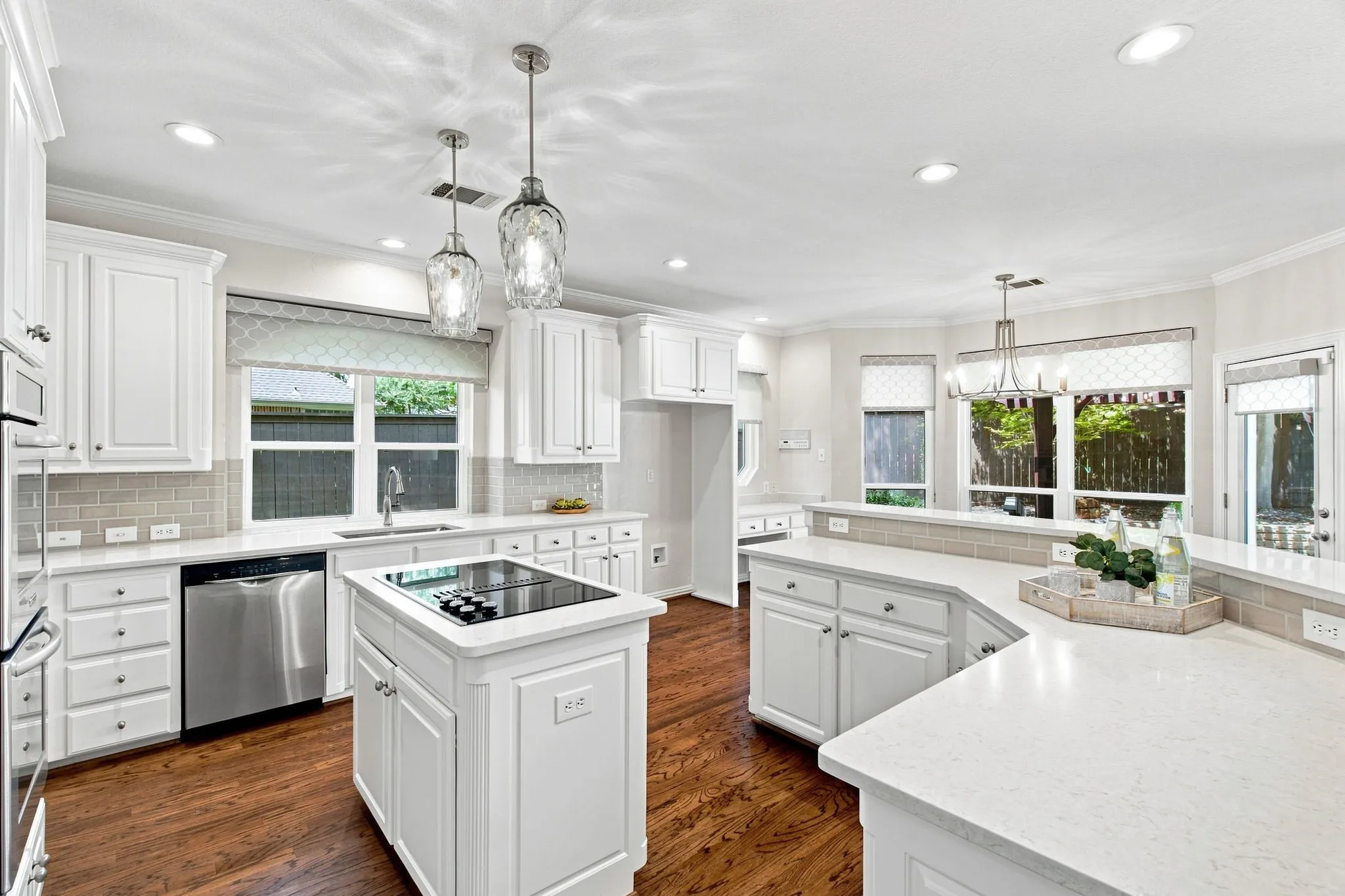White cabinetry, light-toned countertops, wood-finish flooring, stainless steel appliances, and an integrated cooktop