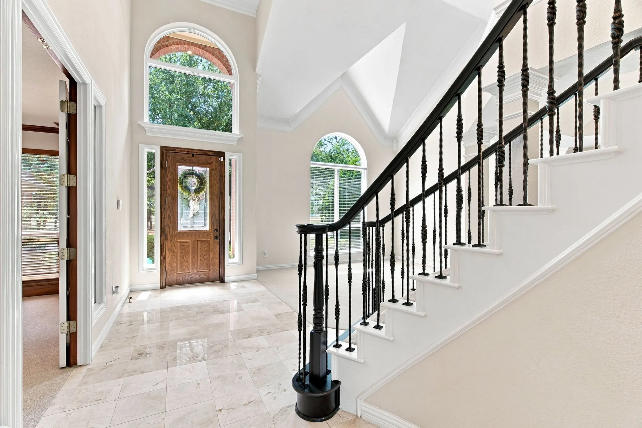 Voluminous entry with high ceilings, arched windows, grand staircase featuring wrought iron balusters, and polished tile flooring