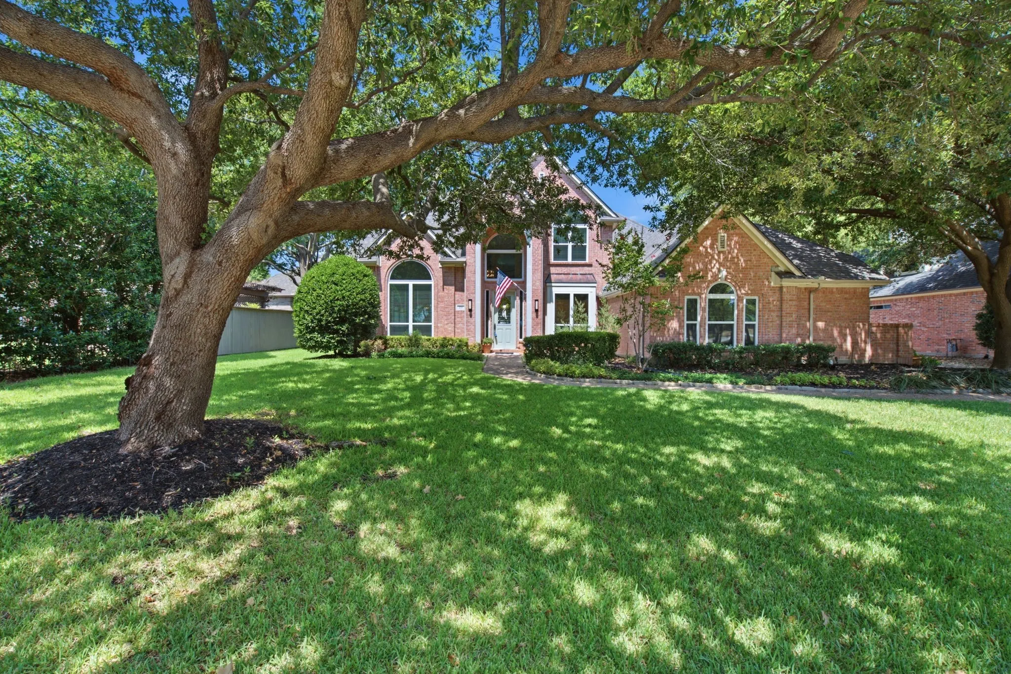 Brick exterior residence featuring a gabled roofline, an arched window, and established landscaping