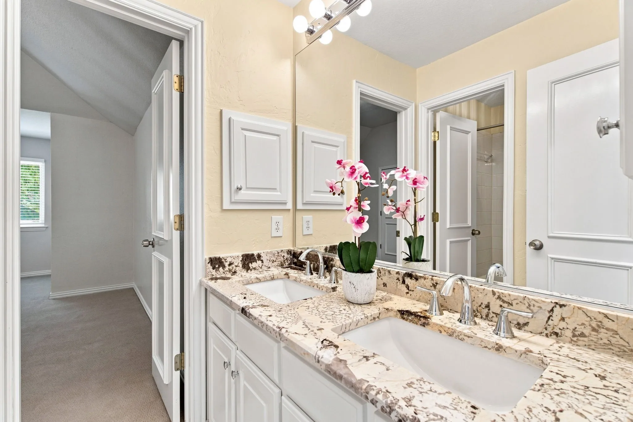 Dual undermount sinks with chrome fixtures, granite countertop, white vanity cabinetry, and mirrored medicine cabinets