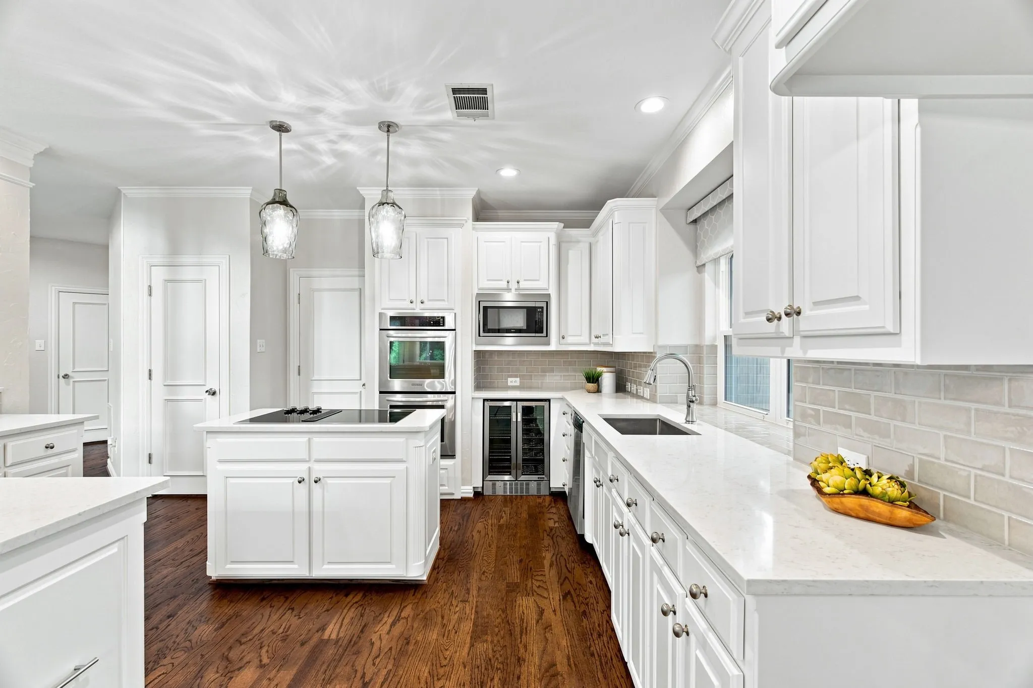 Bright kitchen featuring an island with a built-in cooktop, white cabinetry, integrated stainless steel appliances, light countertops, and wood-finish flooring