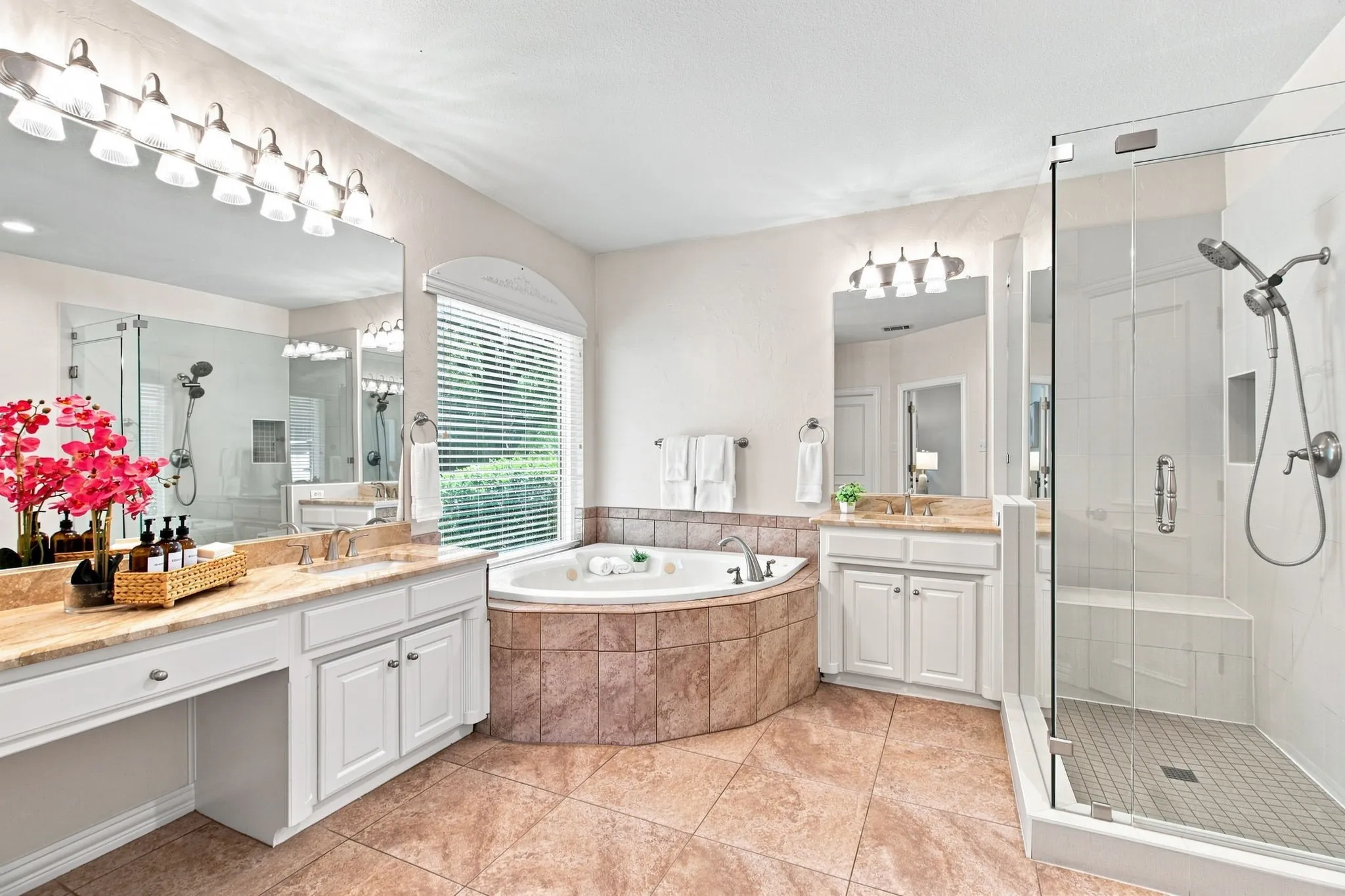 Dual vanity with integrated cabinetry, corner soaking tub, separate glass-enclosed shower with bench, and tiled flooring