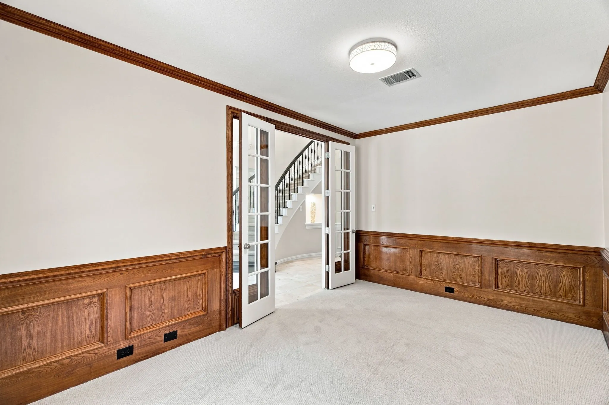 Wood paneling with decorative trim, wood-finish crown molding, French doors with glass panes, and plush carpet flooring