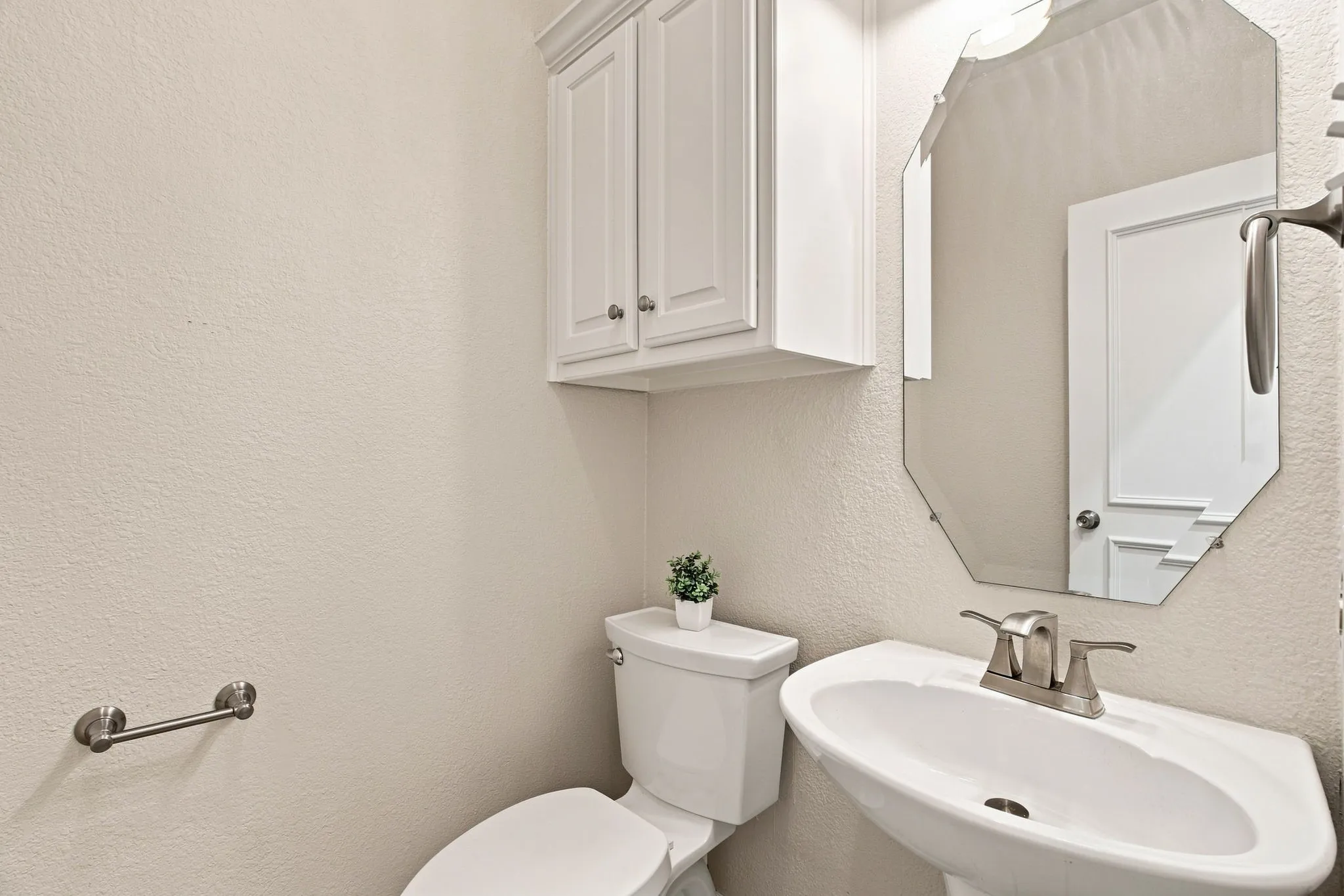 Pedestal sink with a brushed nickel faucet, an octagonal mirror, white wall-mounted cabinetry, and a white toilet
