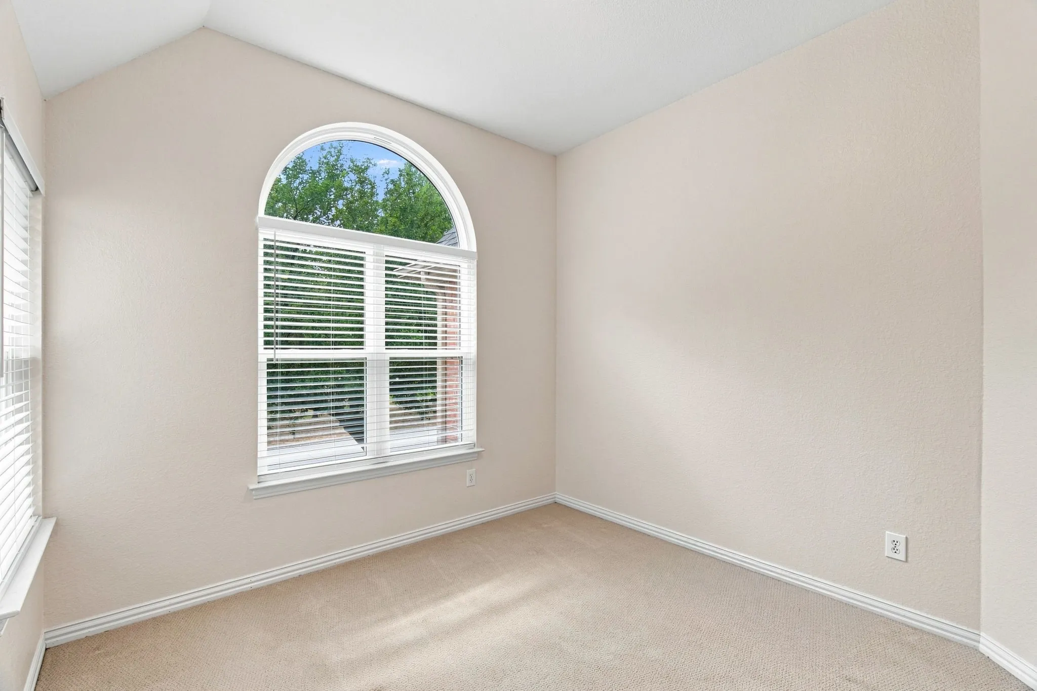 Vaulted ceiling, arched window, carpet flooring, and neutral wall tones
