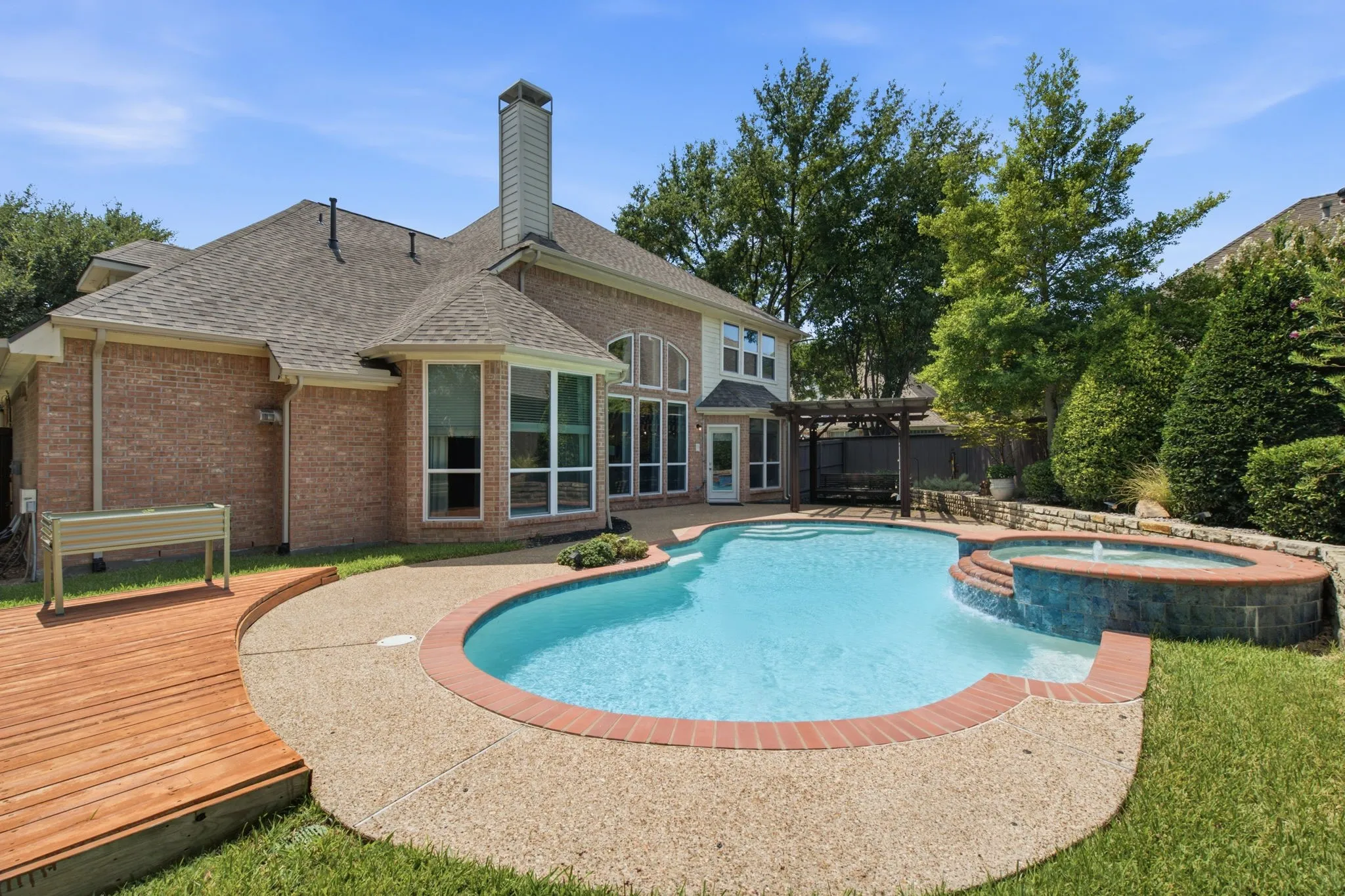 Brick exterior with multiple windows, a swimming pool, and an integrated spa