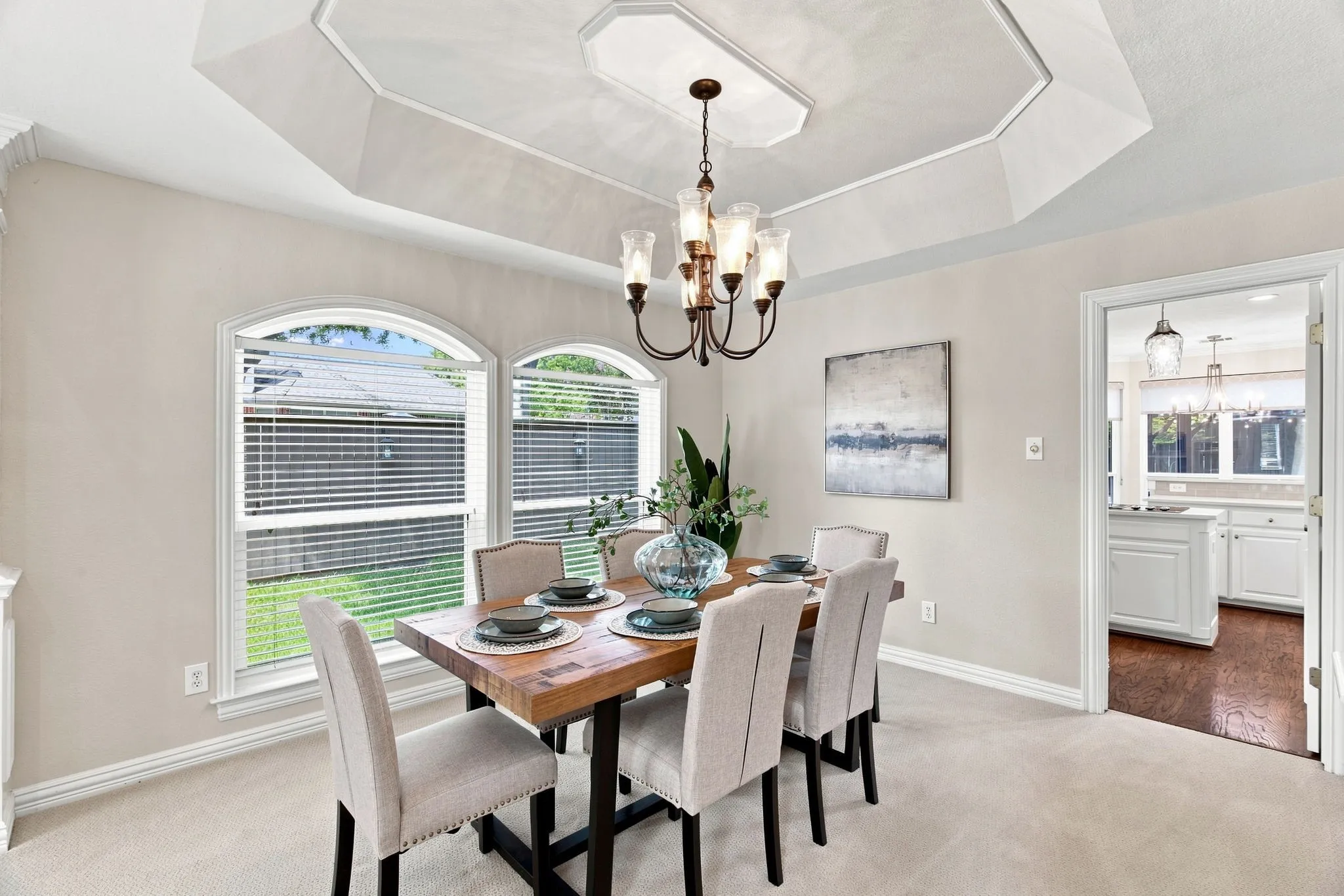 Tray ceiling with crown molding, arched windows, and a multi-light chandelier