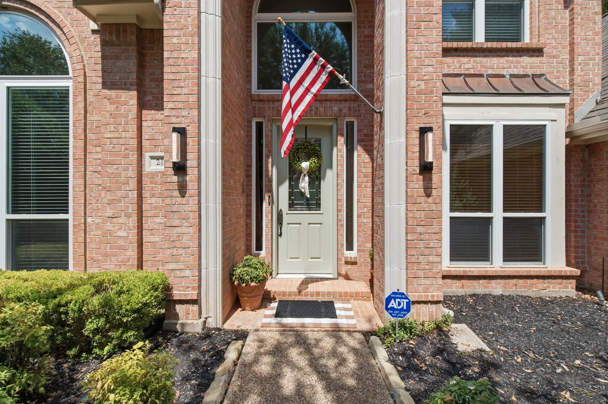 Brick facade with arched windows, light-colored entry door, and exterior sconces flanking the entrance