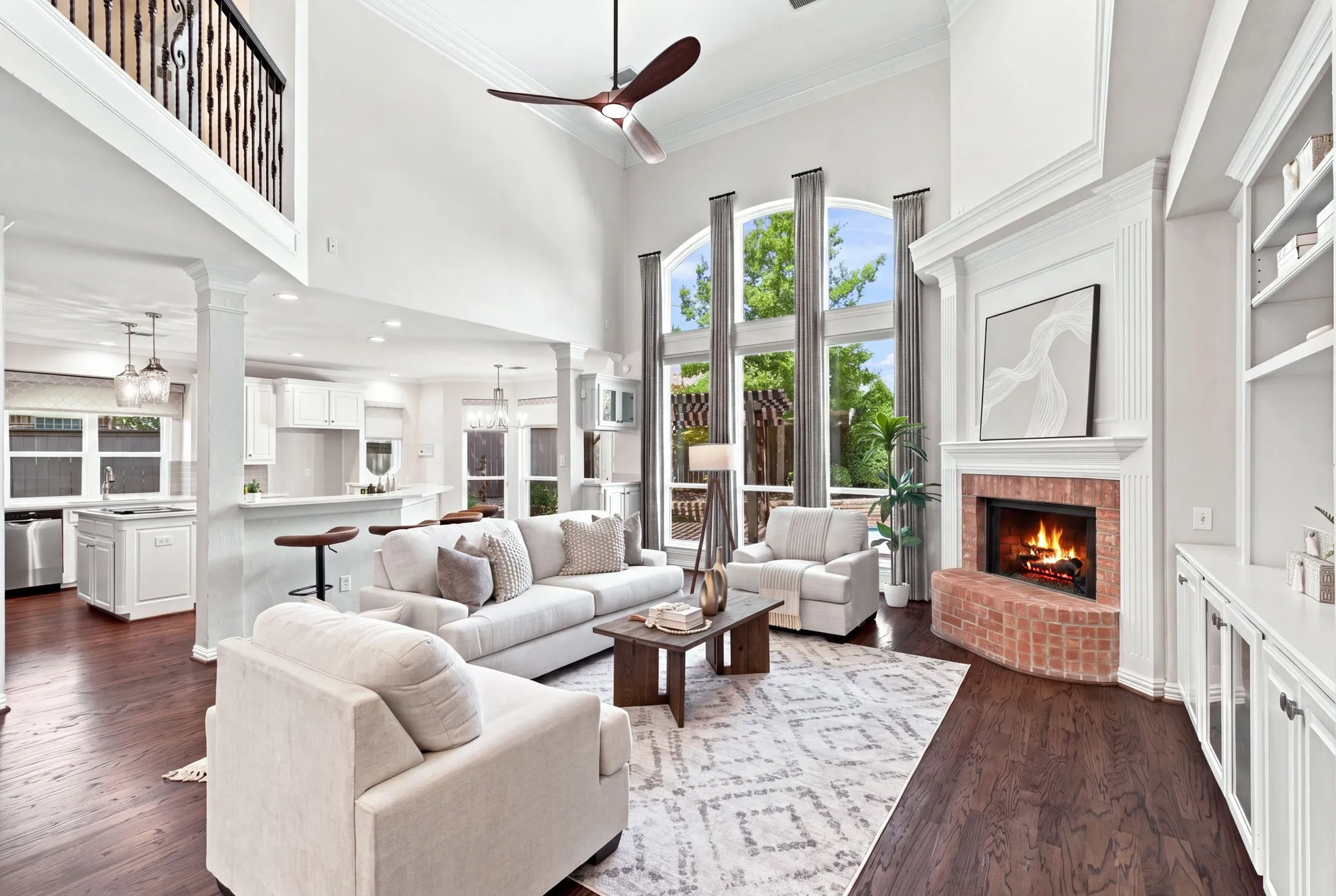 Two-story living area with dark wood-finish flooring, a brick-surround fireplace with a detailed mantel, and built-in shelving