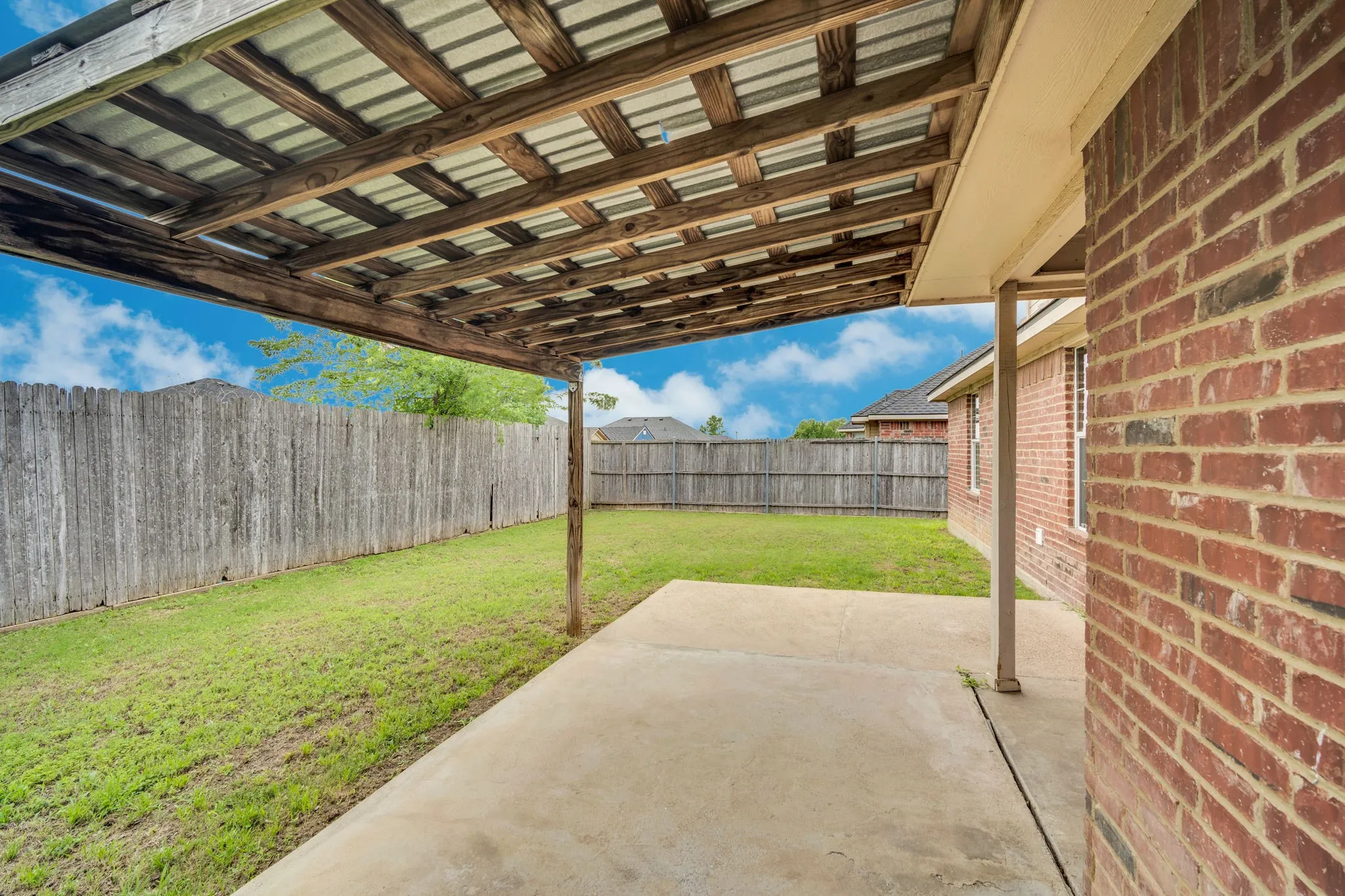 Covered patio with a corrugated metal roof, wood support beams, and a concrete slab