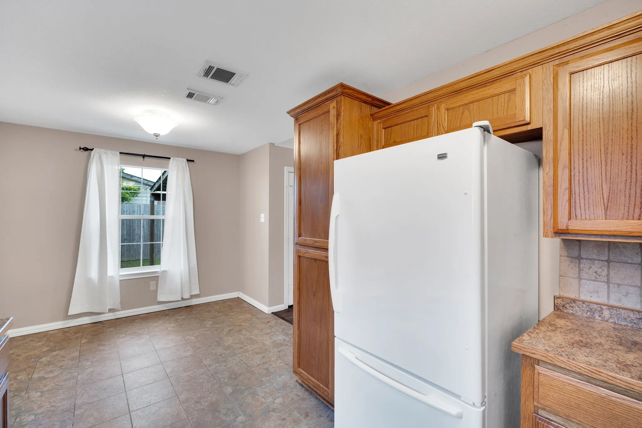 Kitchen area featuring wood-finish cabinetry, tile backsplash, laminate countertops, and resilient tile flooring