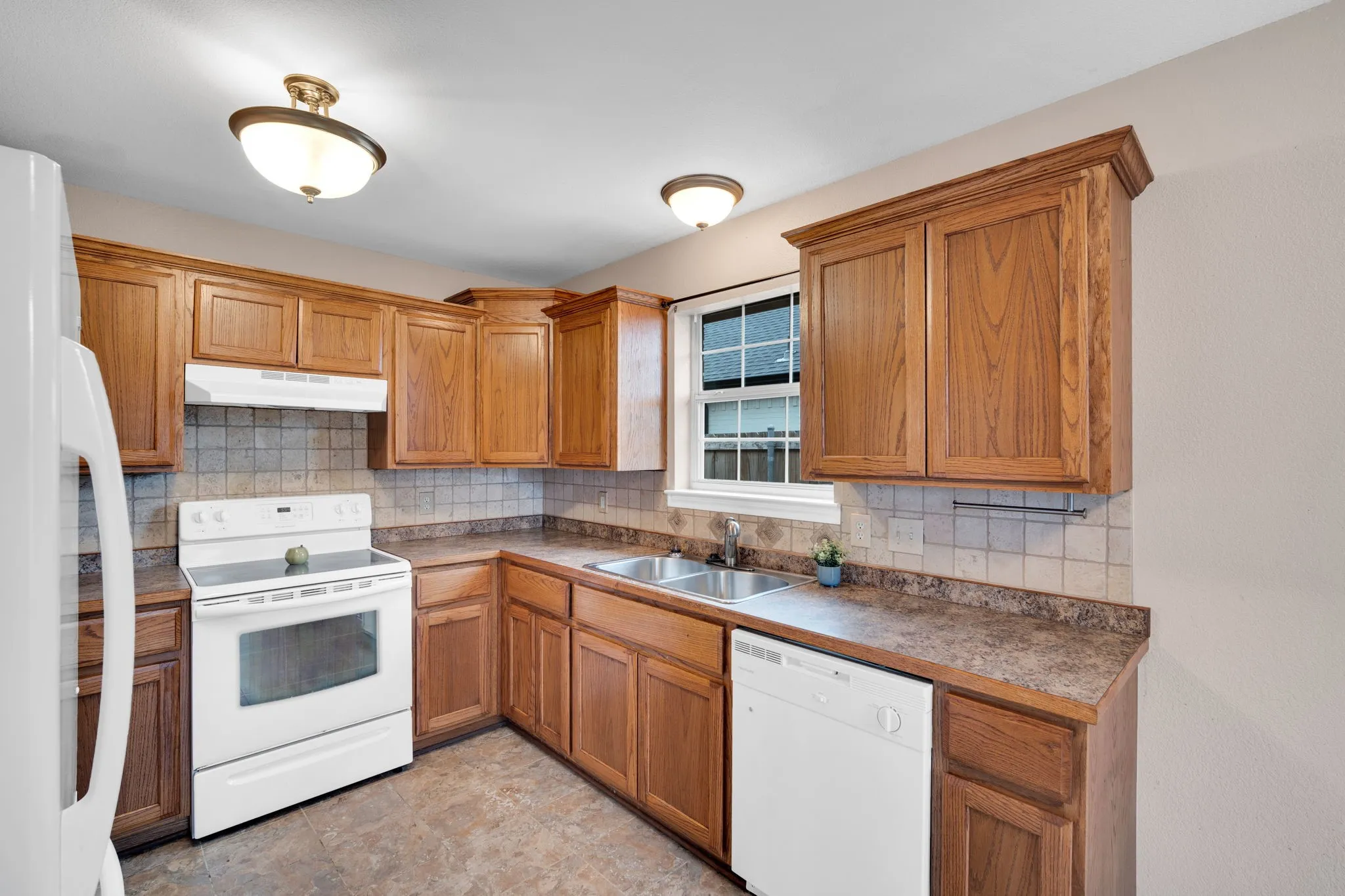 Kitchen featuring wood-finish cabinetry, white appliances, dual basin stainless steel sink, and tile flooring