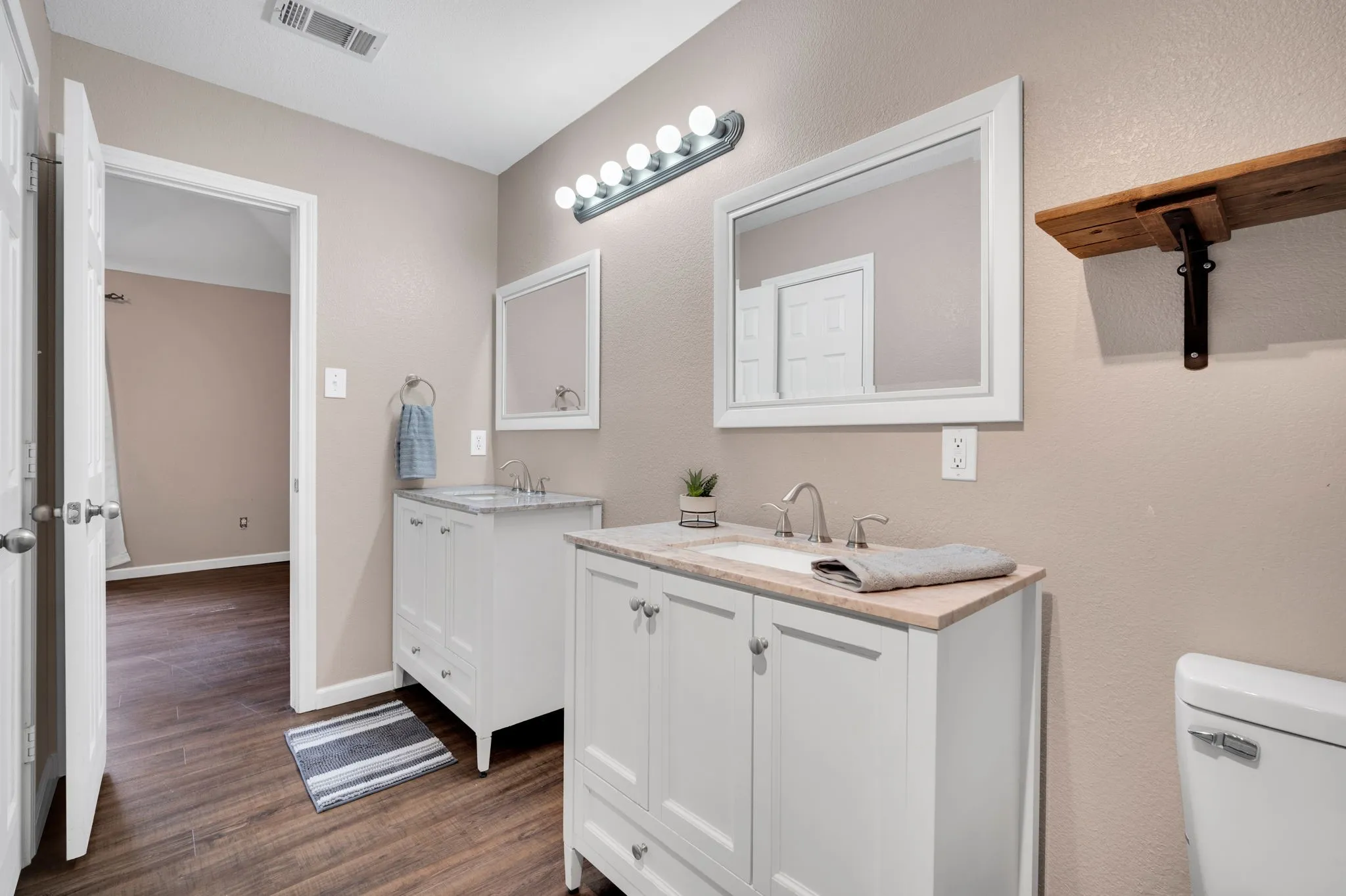 Dual white vanity cabinets with integrated sinks, framed mirrors, and wood-finish flooring
