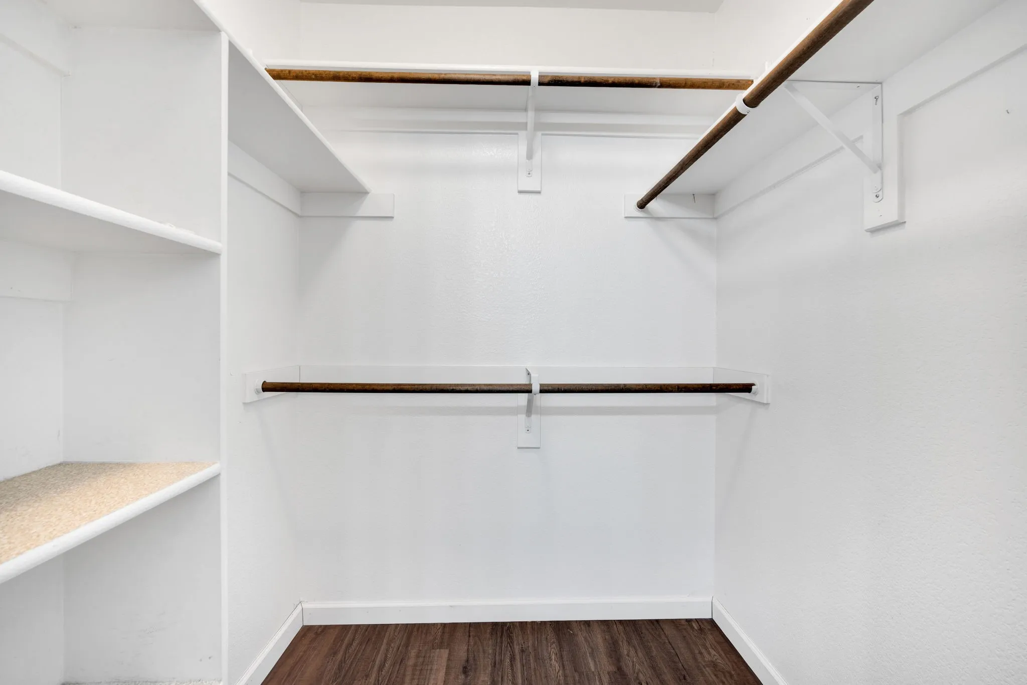 Walk-in closet featuring built-in shelving, multiple hanging rods, and wood-finish flooring