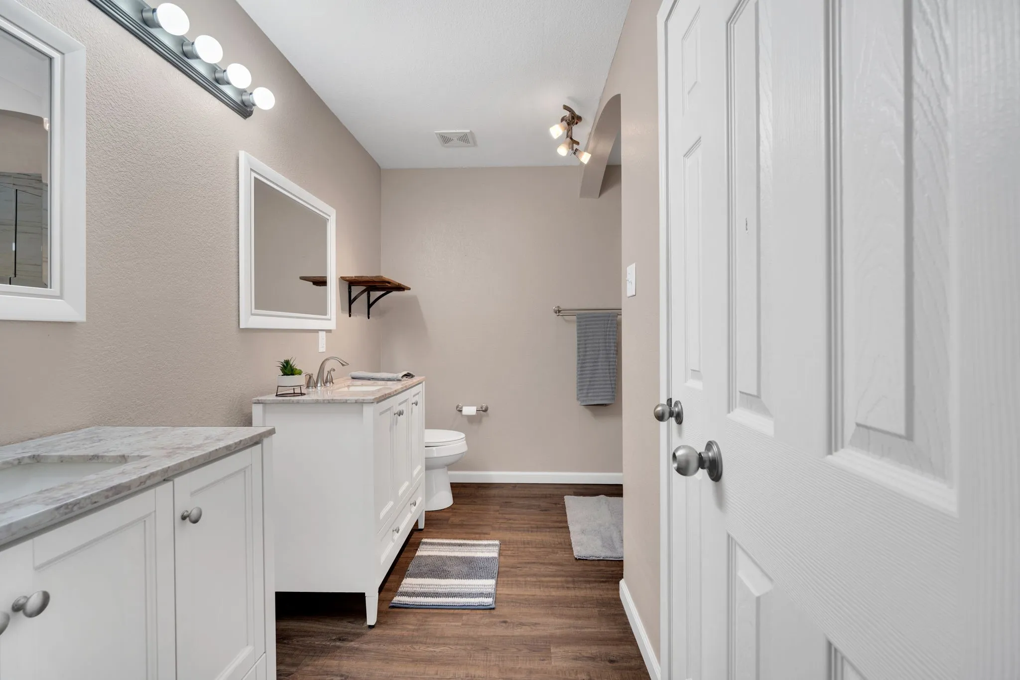Bathroom featuring dual white vanities with integrated sinks, wood-finish flooring, recessed lighting, and a white paneled door