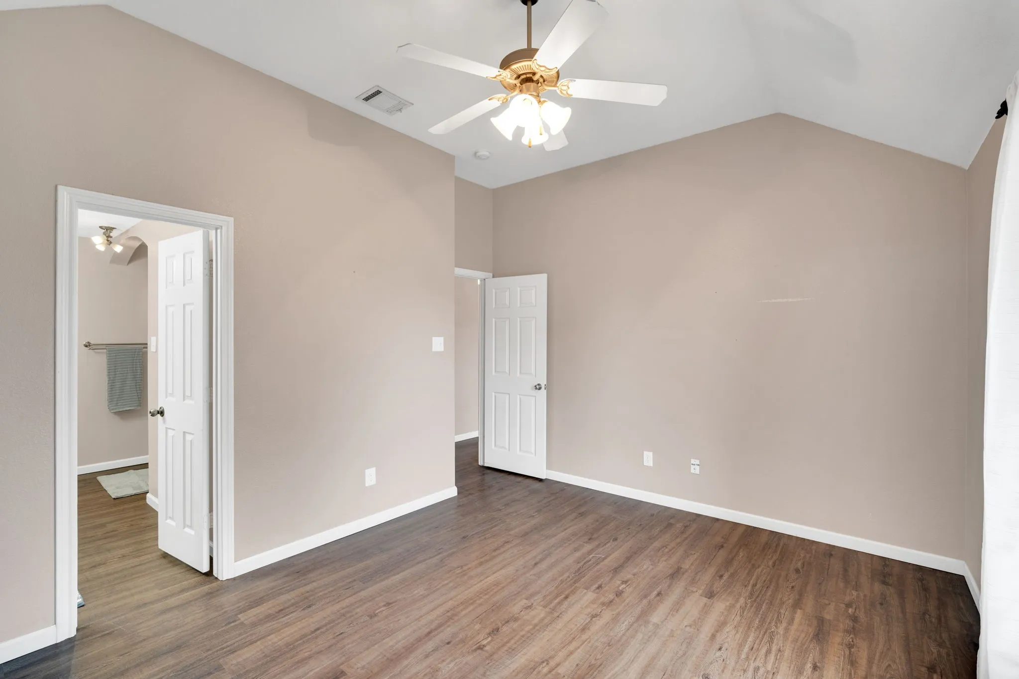 Spacious Primary bedroom featuring vaulted ceilings, wood-finish flooring, and a ceiling fan