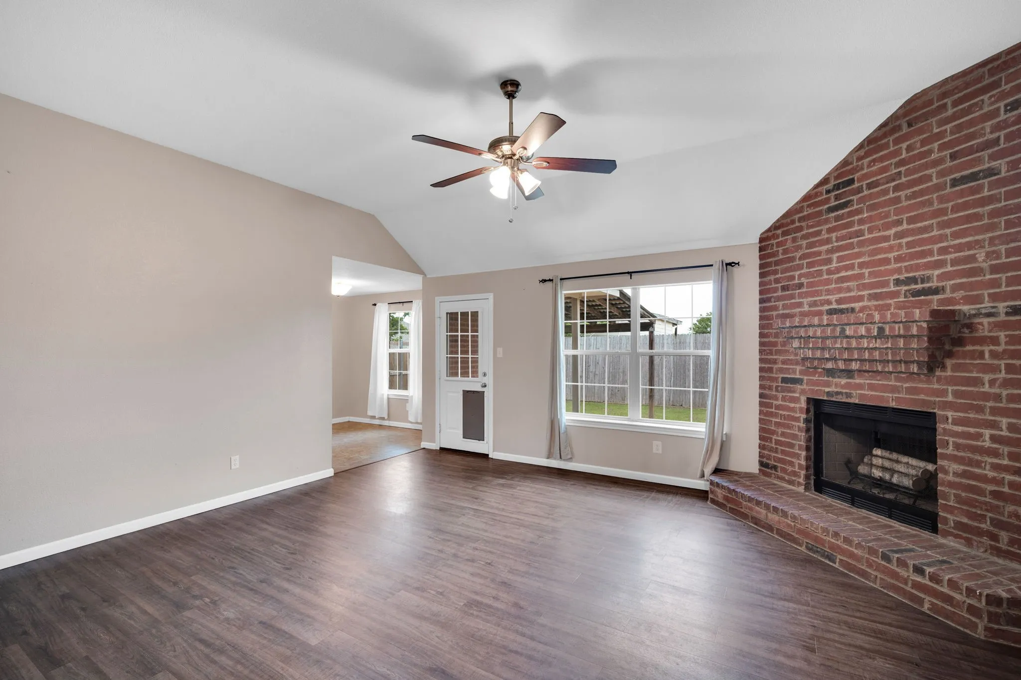 Living area featuring vaulted ceilings, wood-finish flooring, a brick fireplace, a ceiling fan, and multiple windows