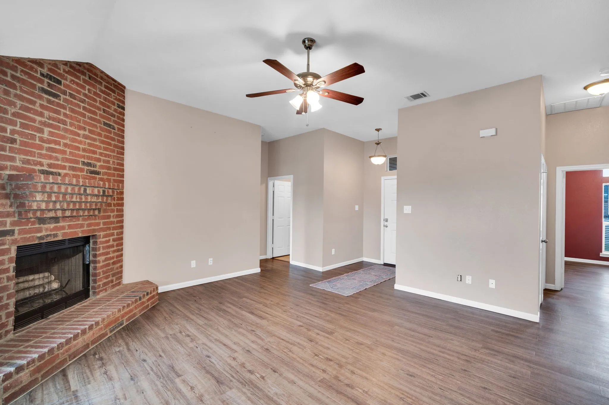 Living area featuring a brick fireplace with hearth, wood-finish flooring, vaulted ceiling, and a ceiling fan with integrated lighting