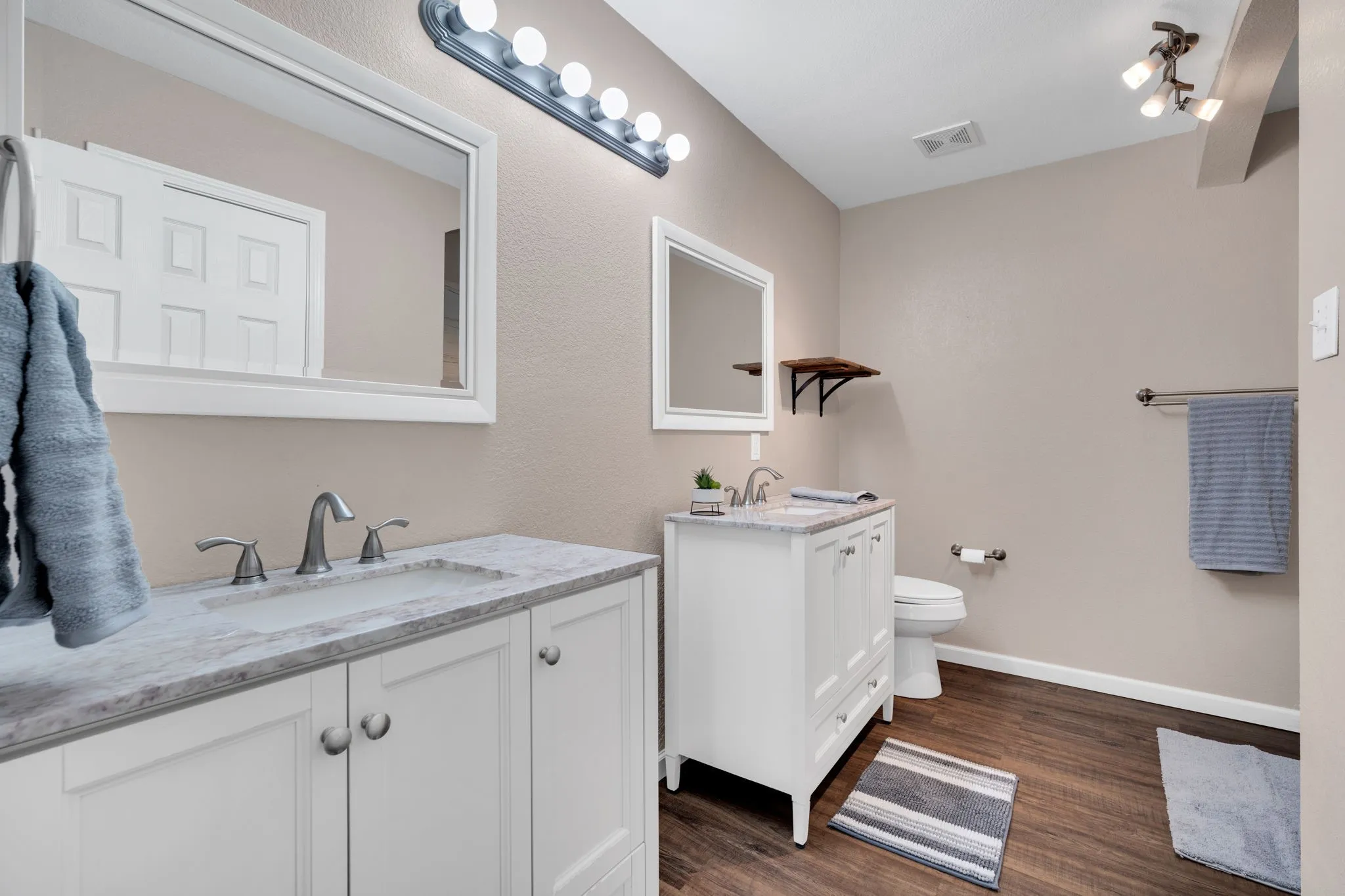 Bathroom featuring dual white vanity cabinets with integrated sinks and stone countertops