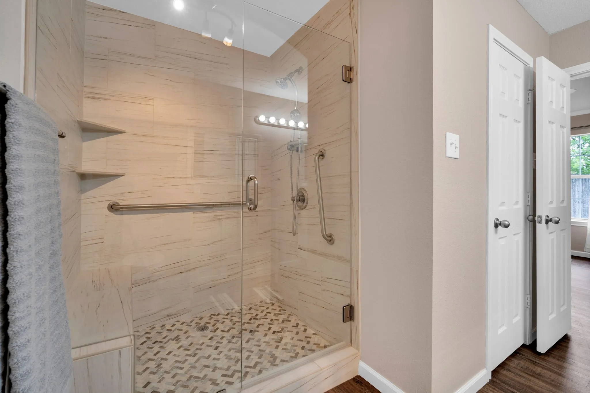 Glass-enclosed shower featuring white-toned tile walls, built-in shelving, a shower bench, and a mosaic tile floor