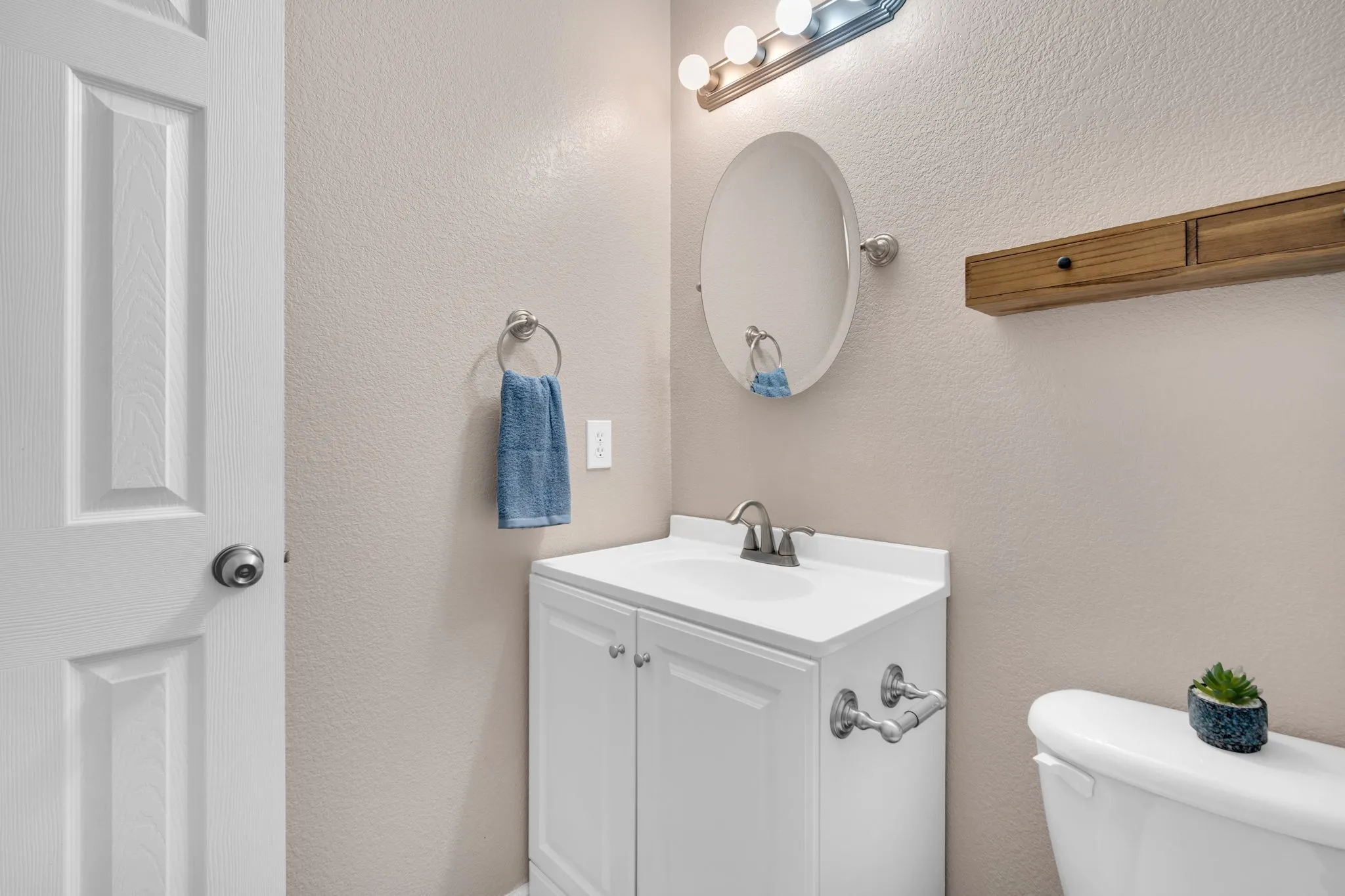 Bathroom vanity with white cabinetry and integrated sink, brushed nickel faucet, and coordinating oval mirror