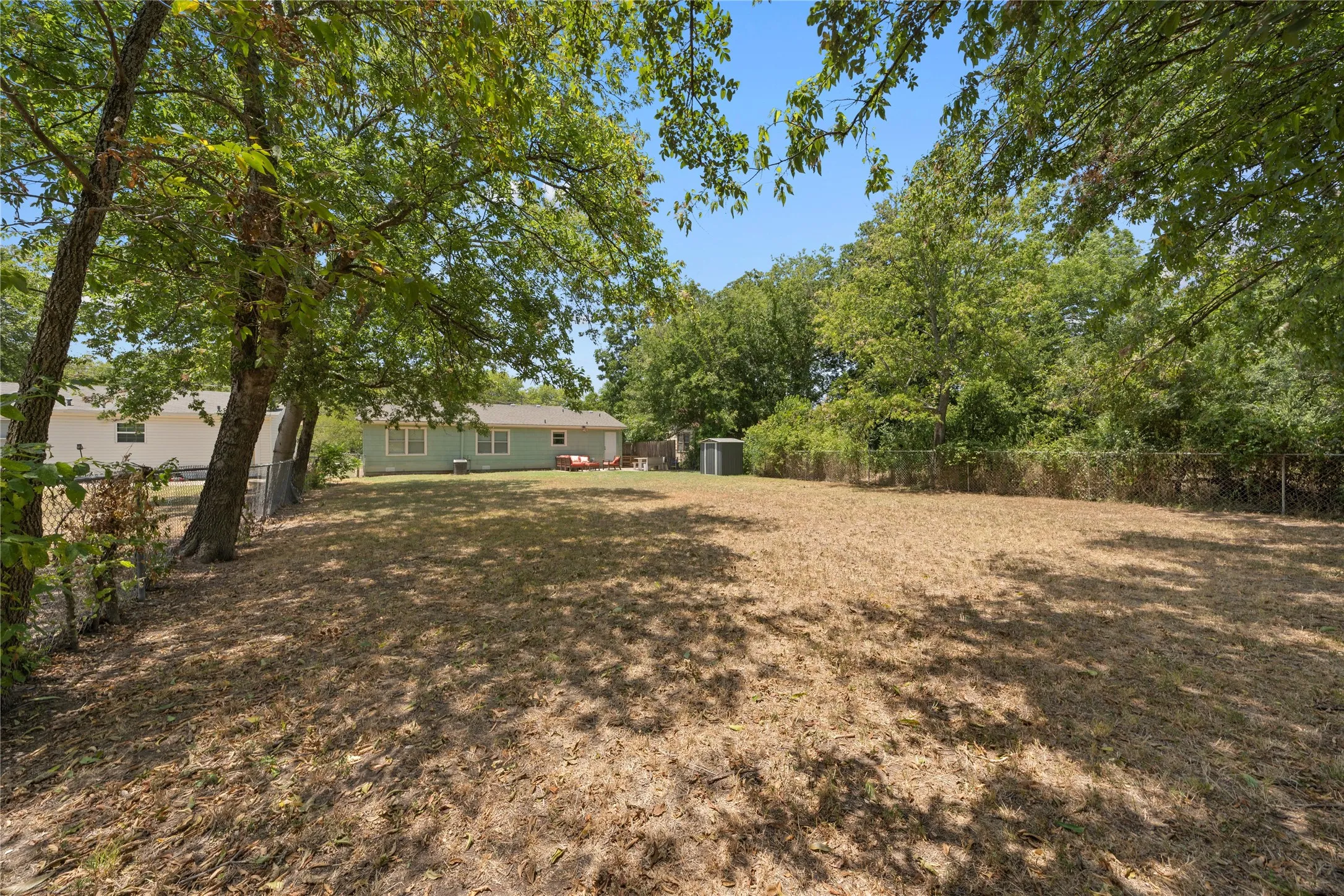 Expansive backyard featuring mature trees, chain-link fencing, a storage shed, and ample space