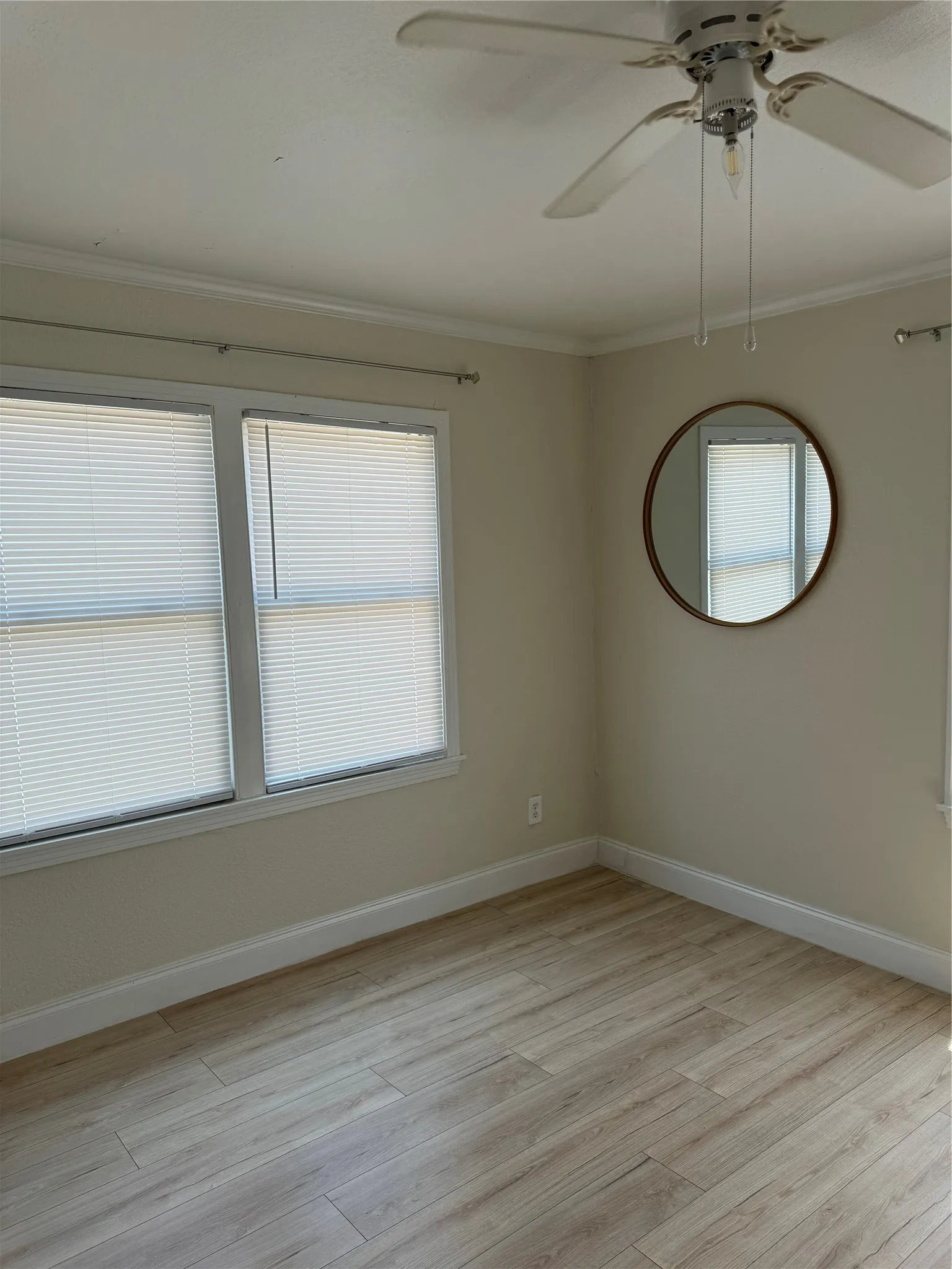 Wood-finish flooring with white baseboards, crown molding, and a ceiling fan
