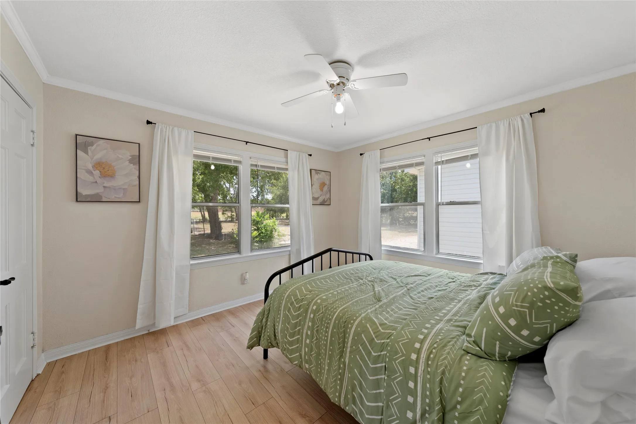 Bedroom featuring light wood-finish flooring, multiple windows with white blinds, crown molding, and a ceiling fan